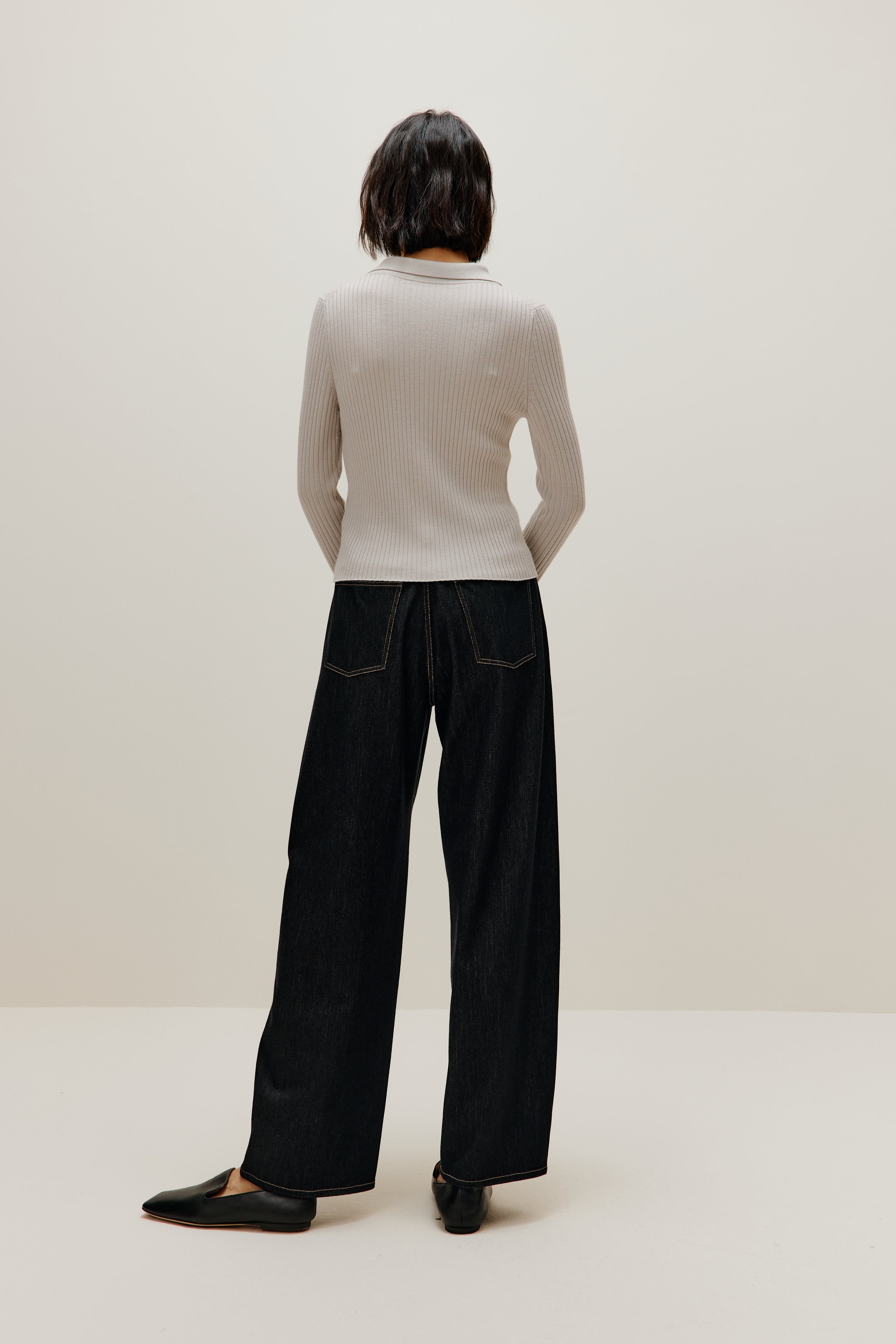 A woman wears a gray silky wool zip-up cardigan and black pants from back