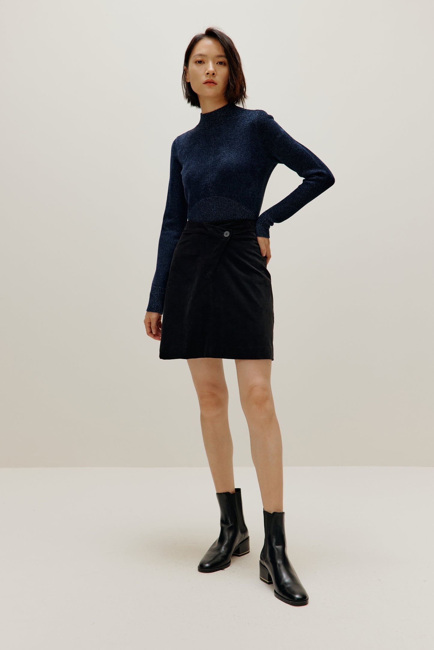 woman wearing blue shimmer mock neck sweater and a black skirt