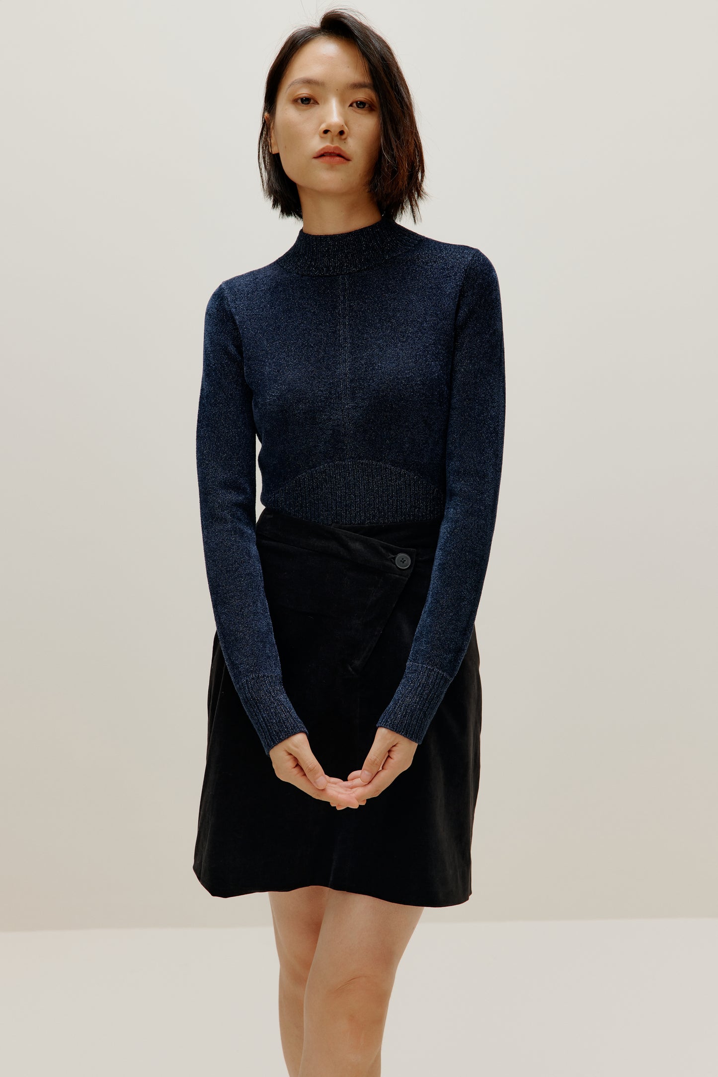 woman wearing blue shimmer mock neck sweater and a black skirt