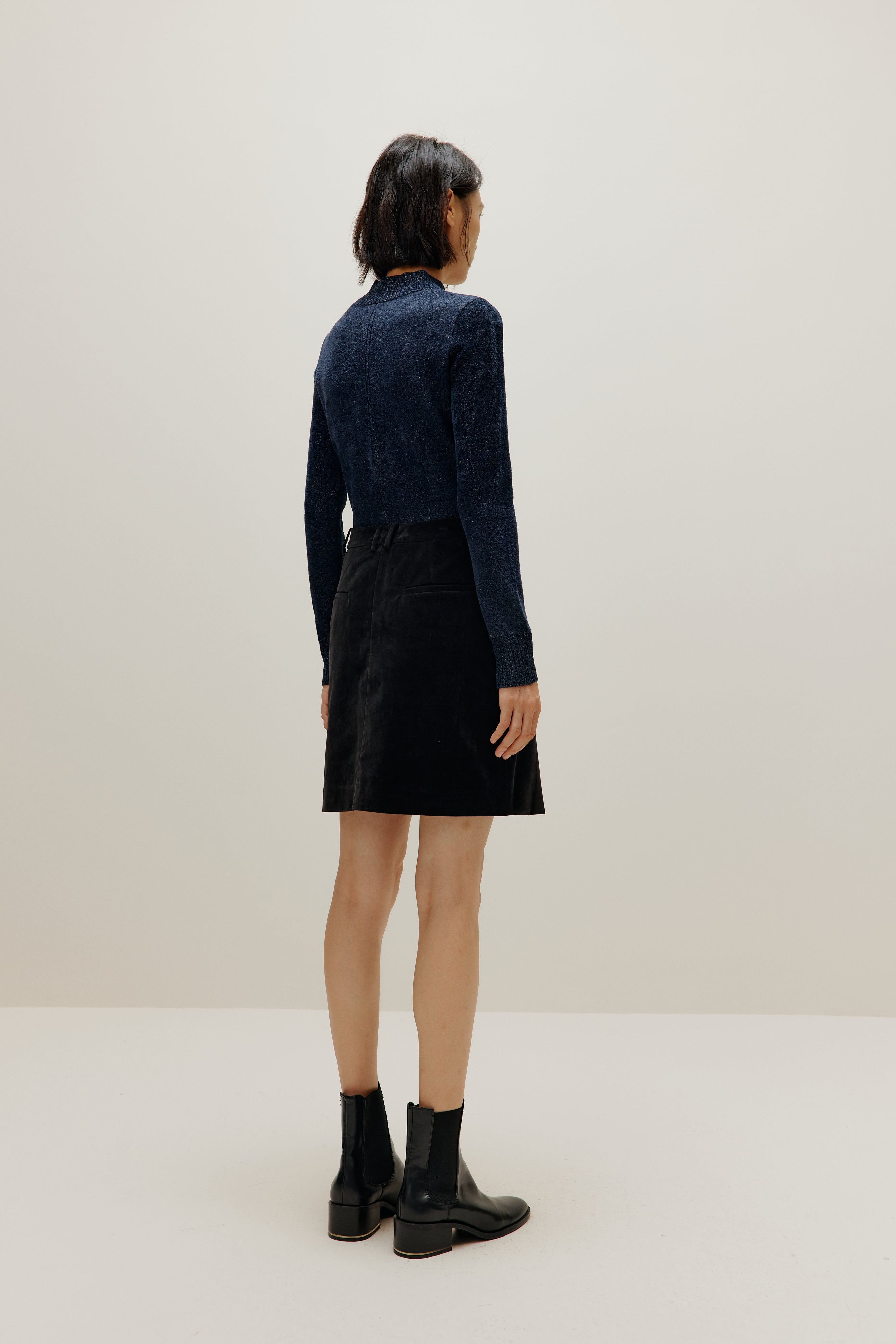woman wearing blue shimmer mock neck sweater and a black skirt