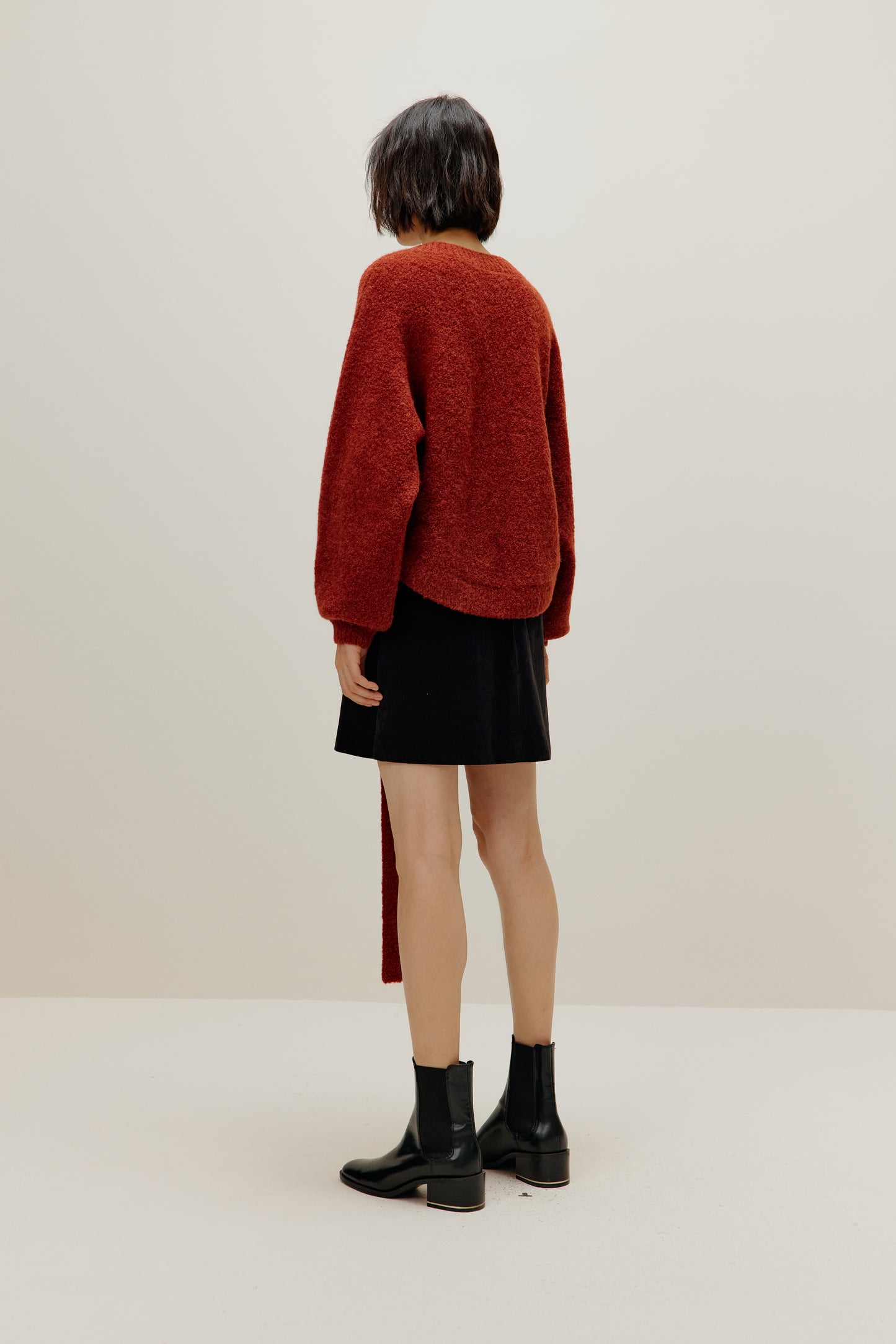 back view of a woman wearing a red wrap cardigan and black skirt