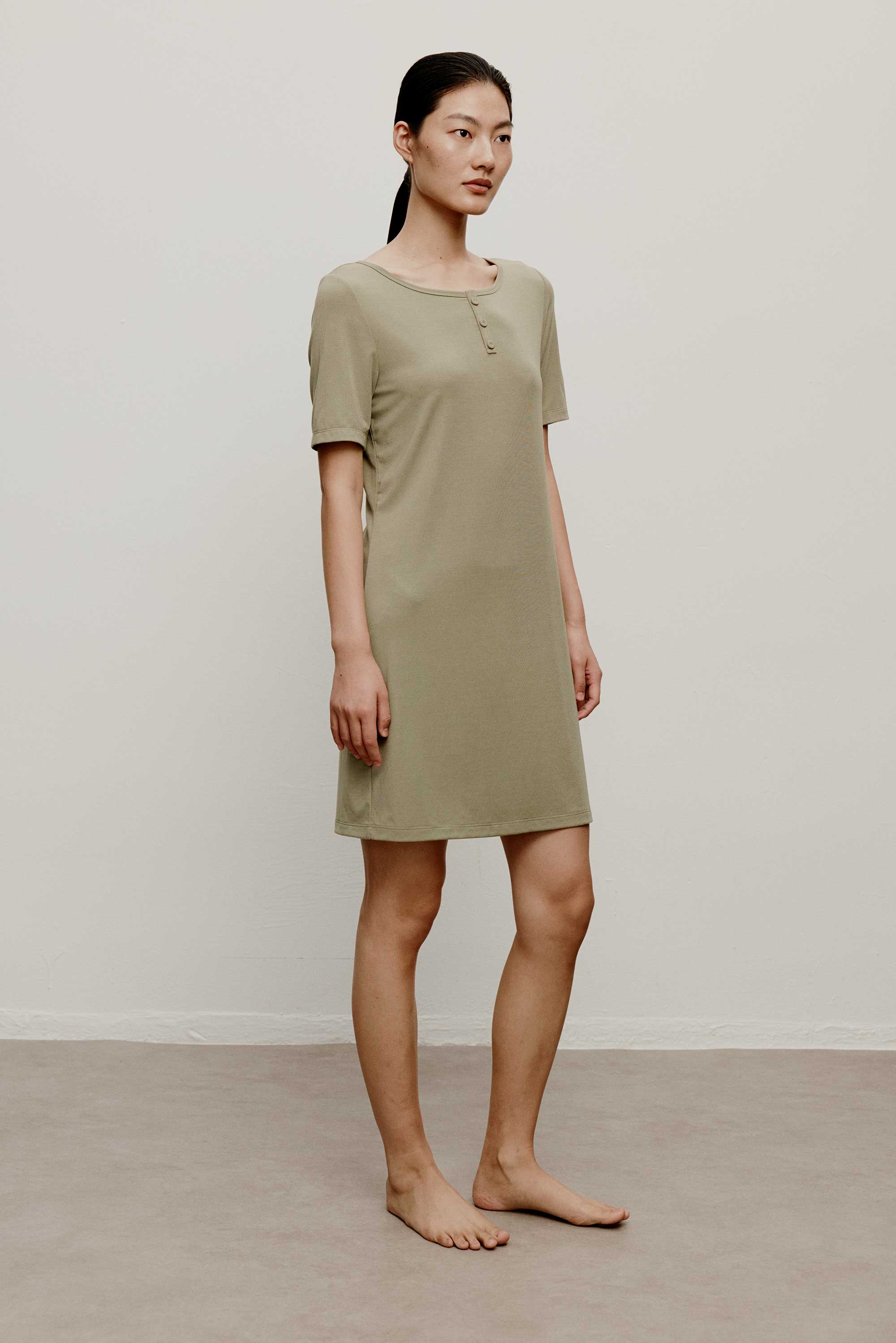 Woman in a green pajama dress, facing right.