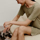 A woman wearing a green pajama dress sitting on the white sofa and petting a puppy.