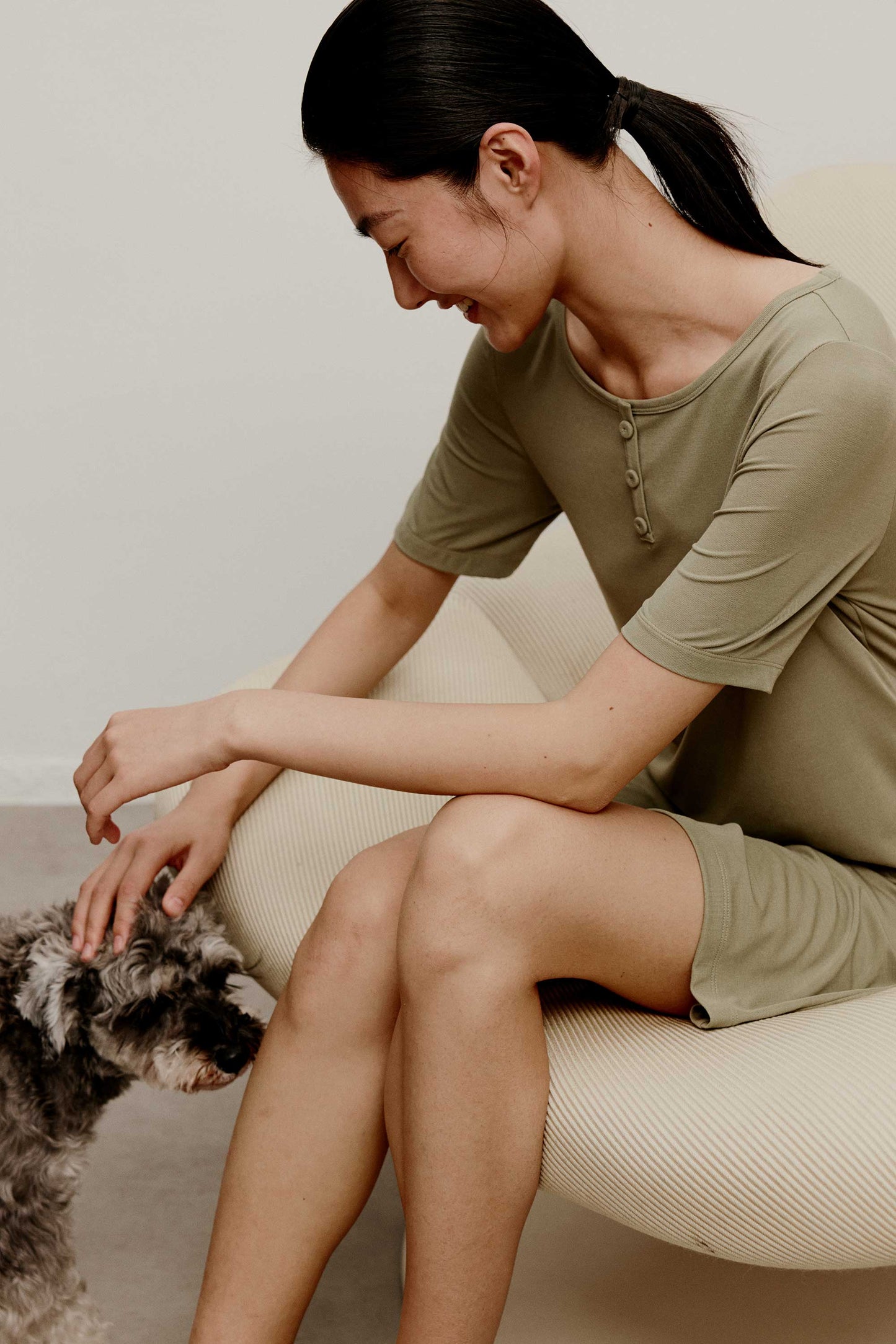 A woman wearing a green pajama dress sitting on the white sofa and petting a puppy.