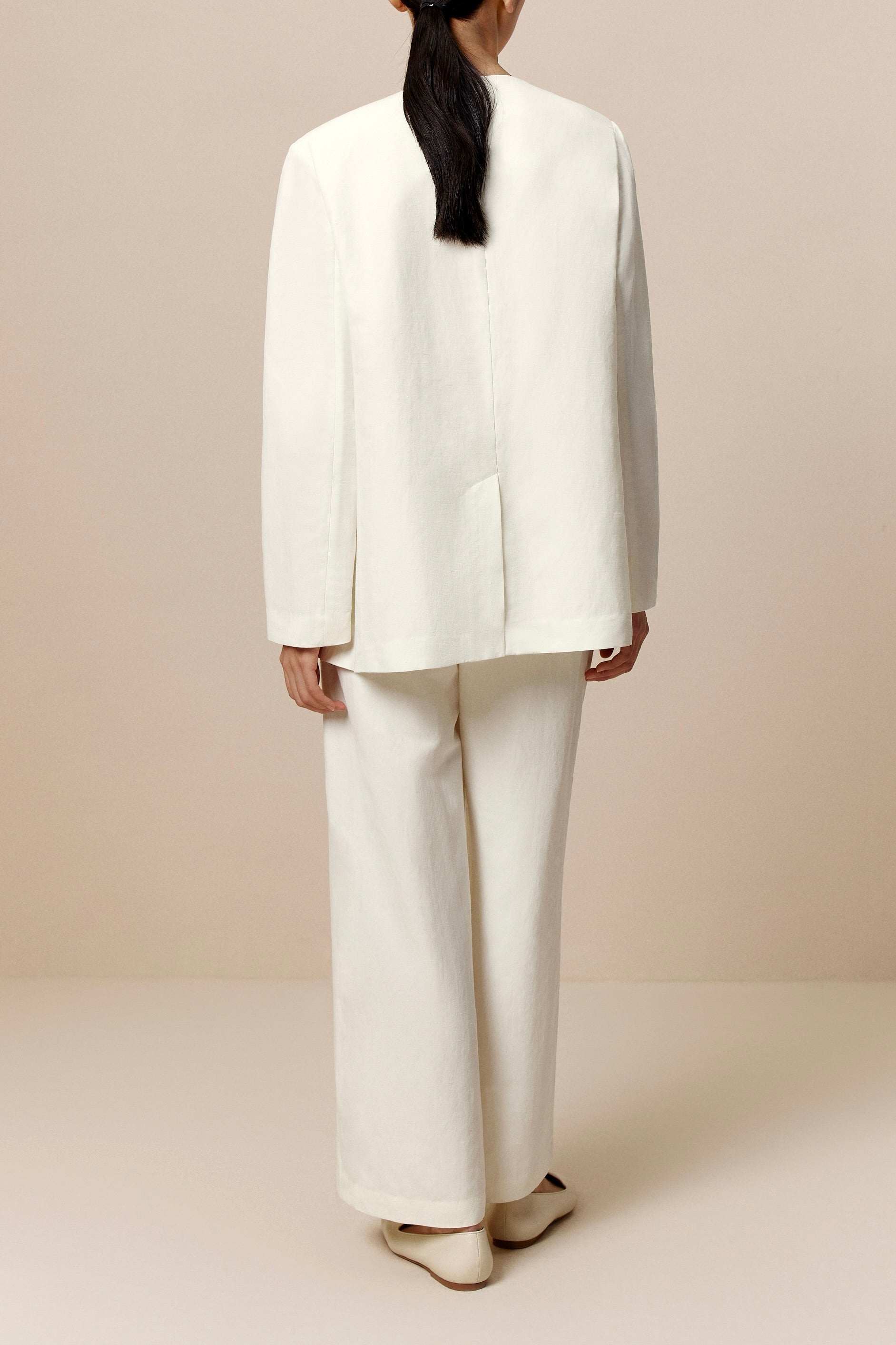 Back view of woman wearing ivory blazer, ivory tank, and ivory pants.