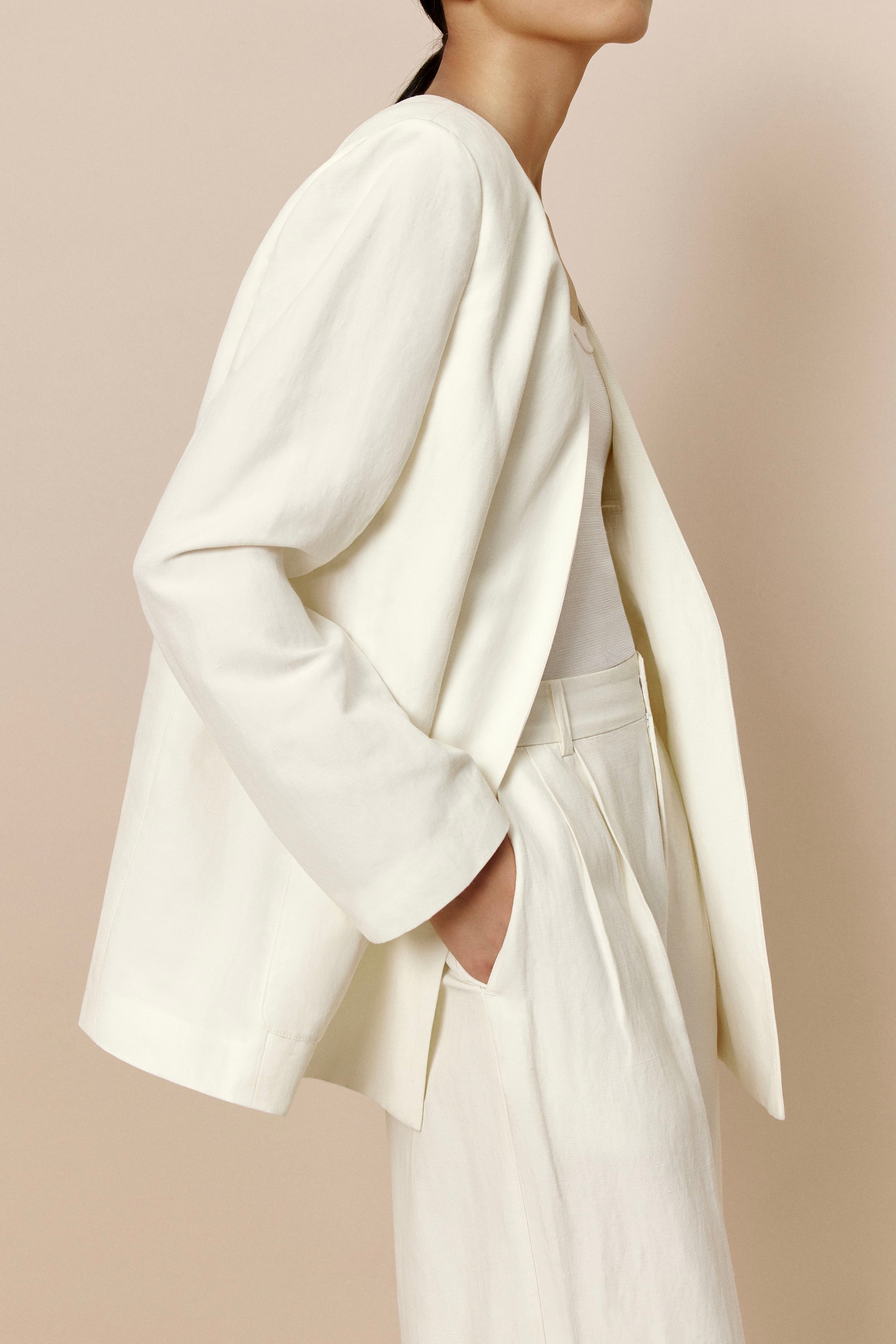 Side view of model wearing ivory blazer with matching color top, and hand inside pant pocket.