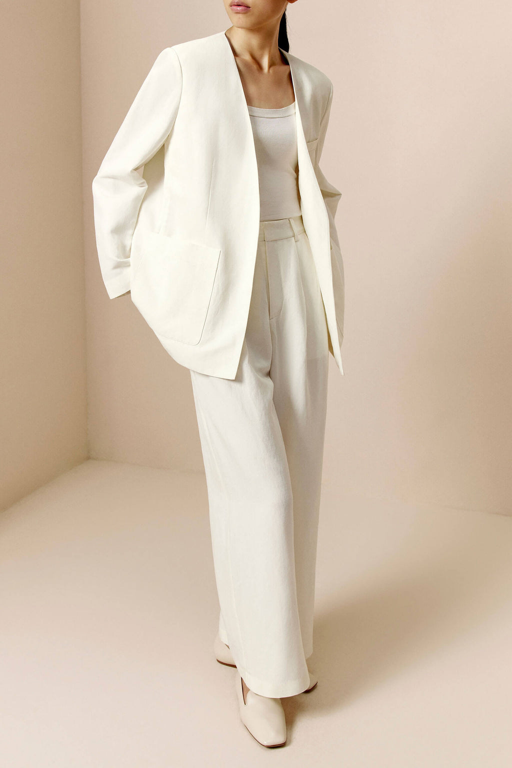Front side view of woman wearing ivory blazer, ivory tank, and ivory pants.