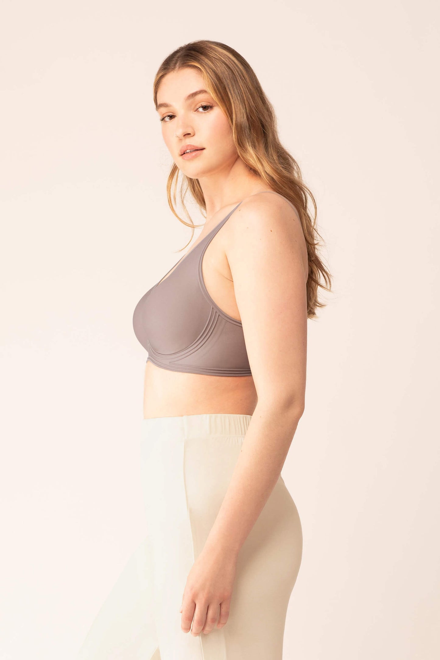 Side view of woman wearing purple grey bra with plunge neckline and white pajama pants
