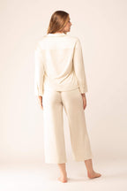 Back view of woman wearing off-white button up pajama shirt and matching pajama bottom