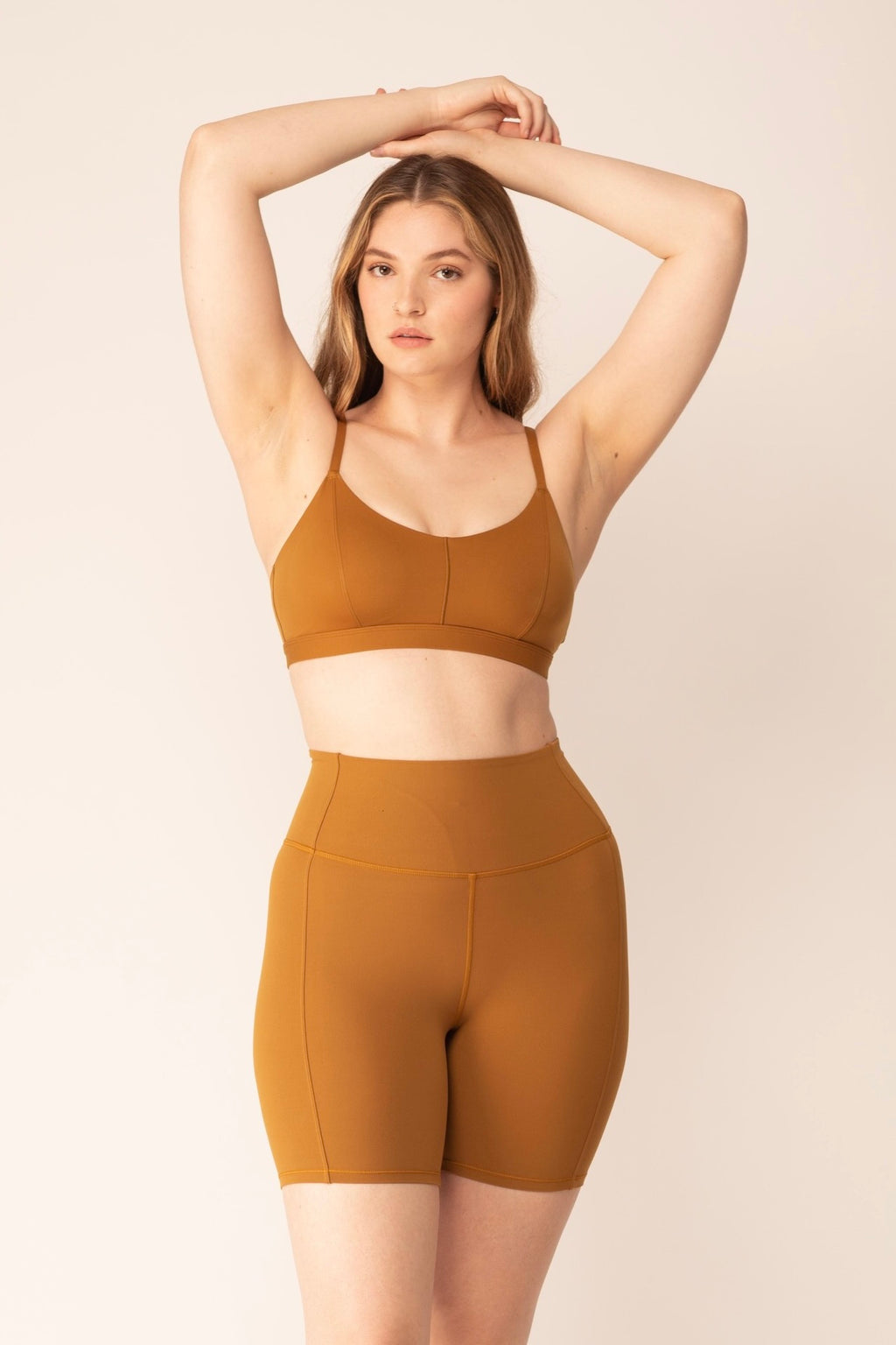 A woman wears a tan sports bra and shorts.