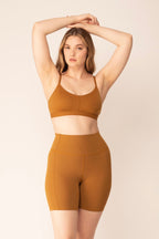A woman wears a tan sports bra and shorts.