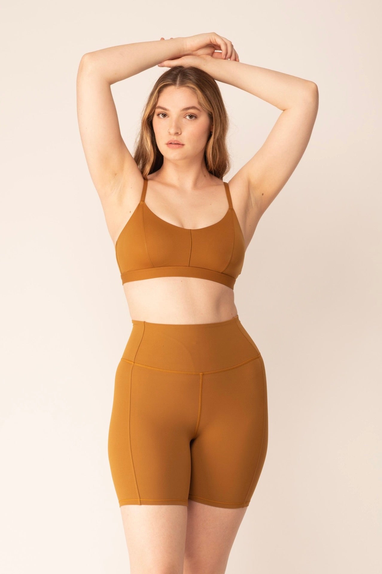 A woman wears a tan sports bra and shorts.