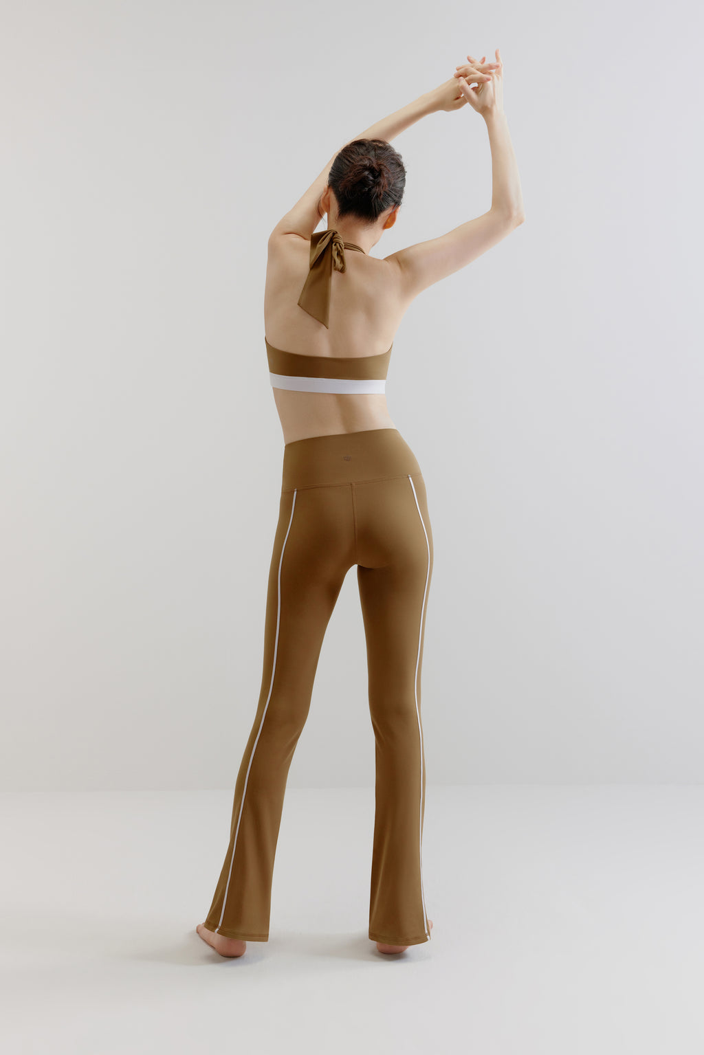 A woman wears an olive green sports bra and flare leggings from back