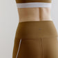 A woman wears an olive green sports bra and leggings from back.