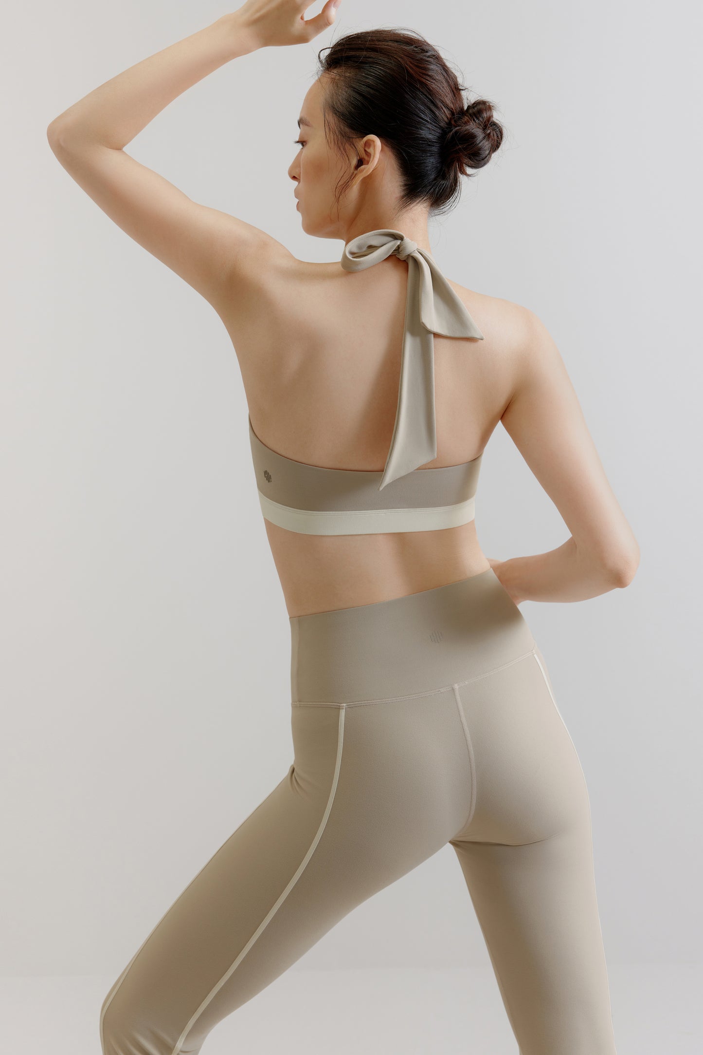A woman wears a gray sports bra and leggings from back.