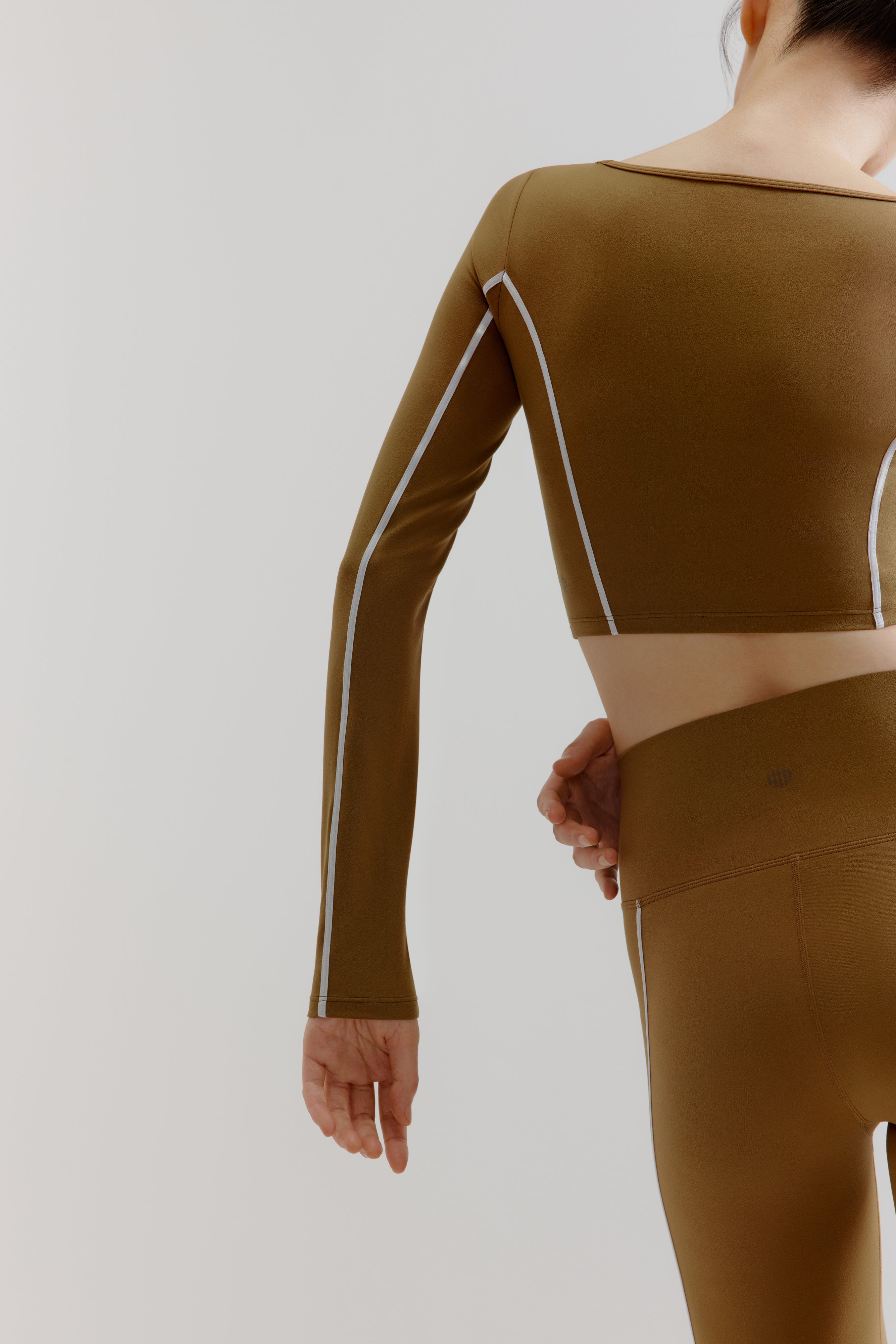 A woman wears an olive green U-Neck Long Sleeve Top and leggings from back.