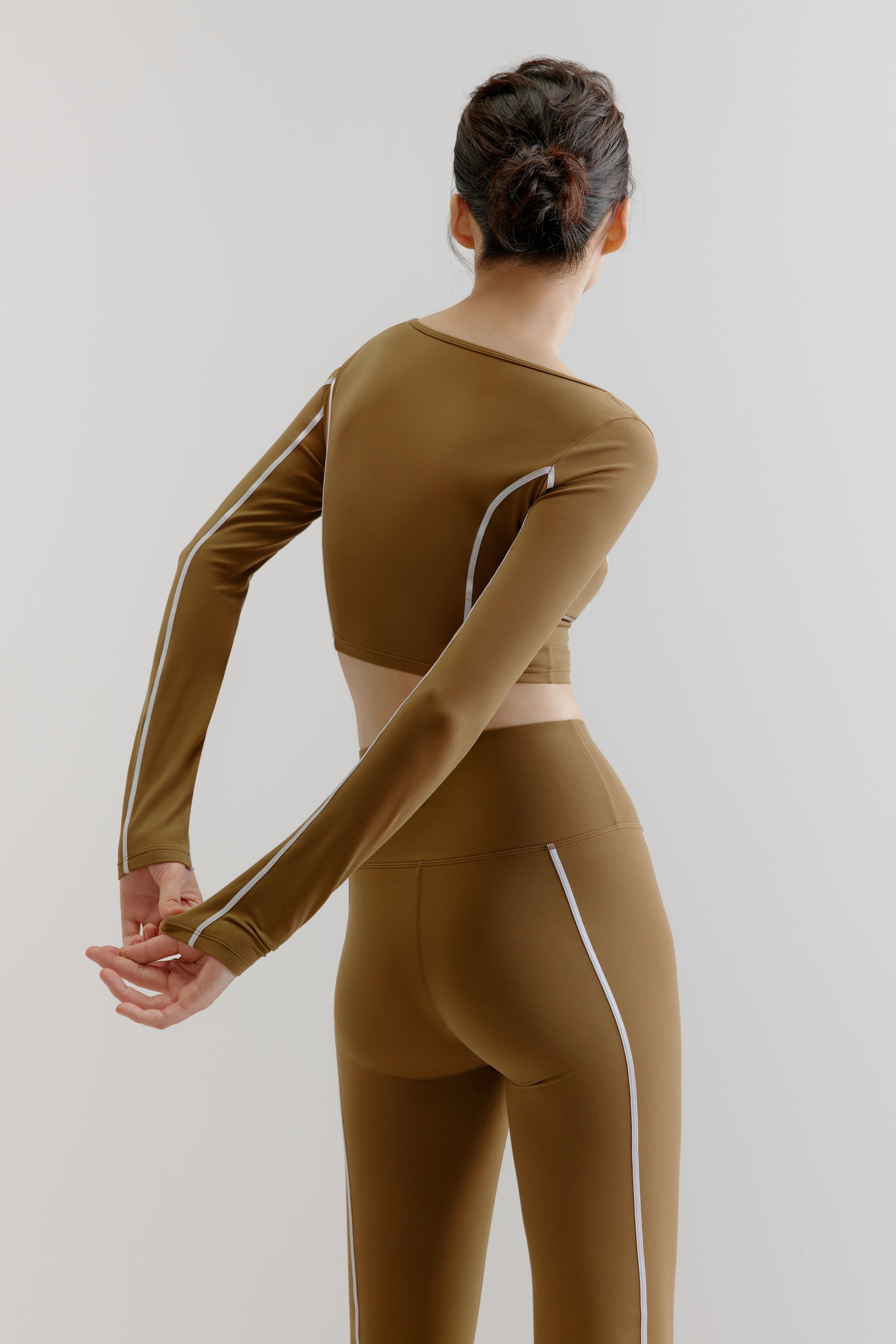A woman wears an olive green U-Neck Long Sleeve Top and leggings from back.