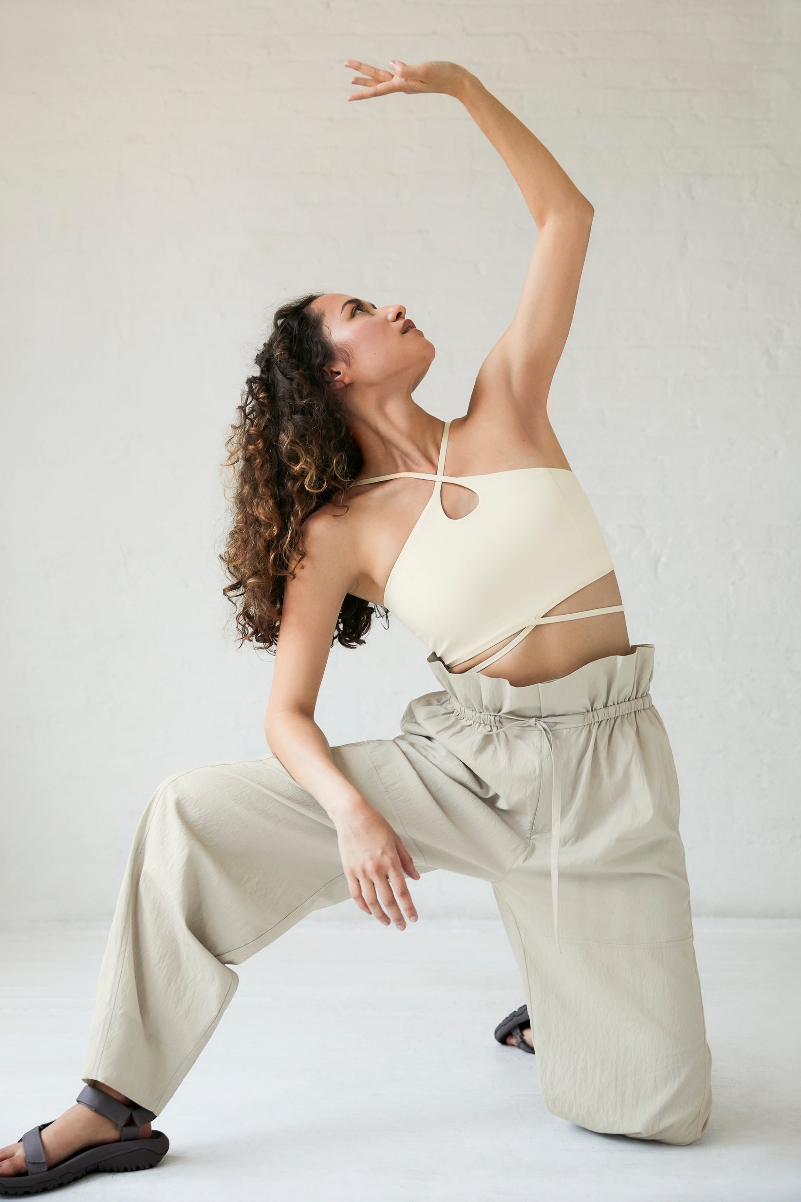 a woman wearing a white sports bra, cream pants and black sandals.  