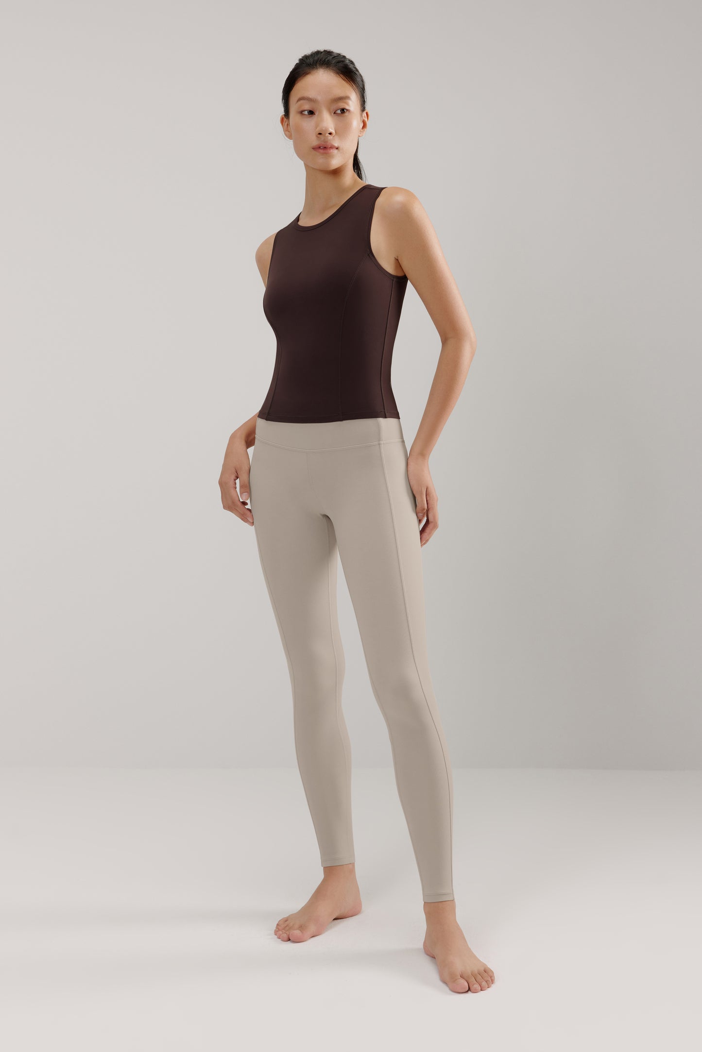 A woman wears a brown tank and cream leggings