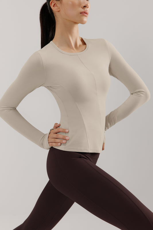 A woman wears a gray mousse long sleeve sports top and brown leggings.