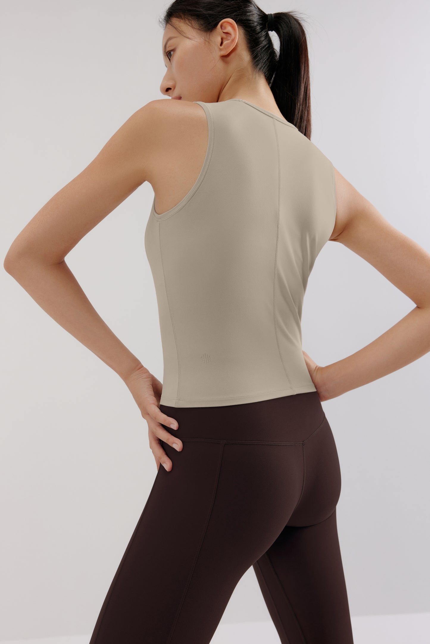 A woman wears a grey tank and brown leggings from back