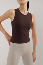 A woman wears a brown tank and cream leggings