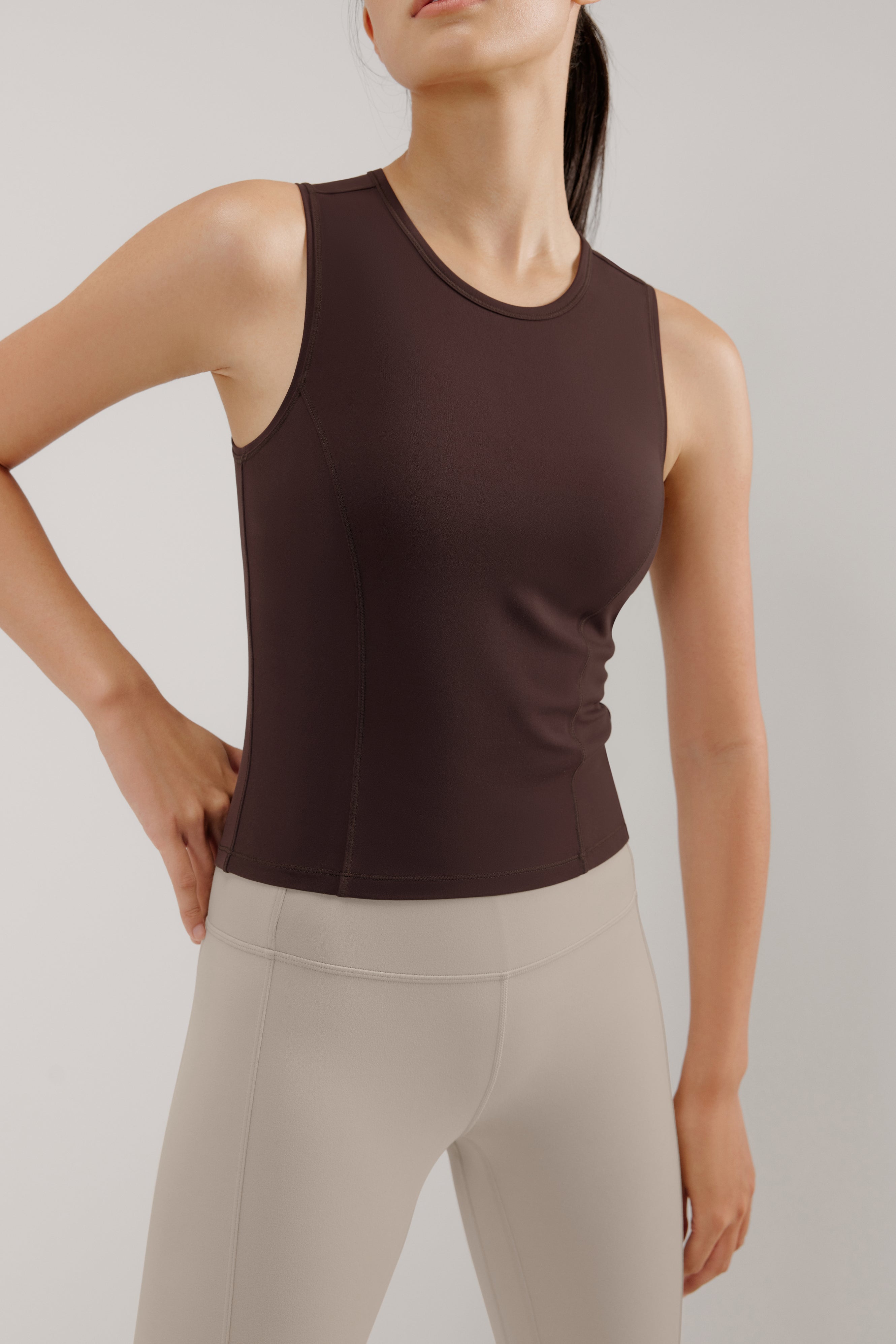 A woman wears a brown tank and cream leggings