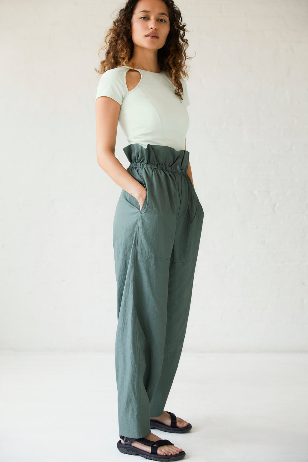 a woman wearing a white top and dark green pants and black sandals.