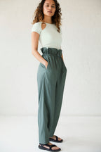 a woman wearing a white top and dark green pants and black sandals.