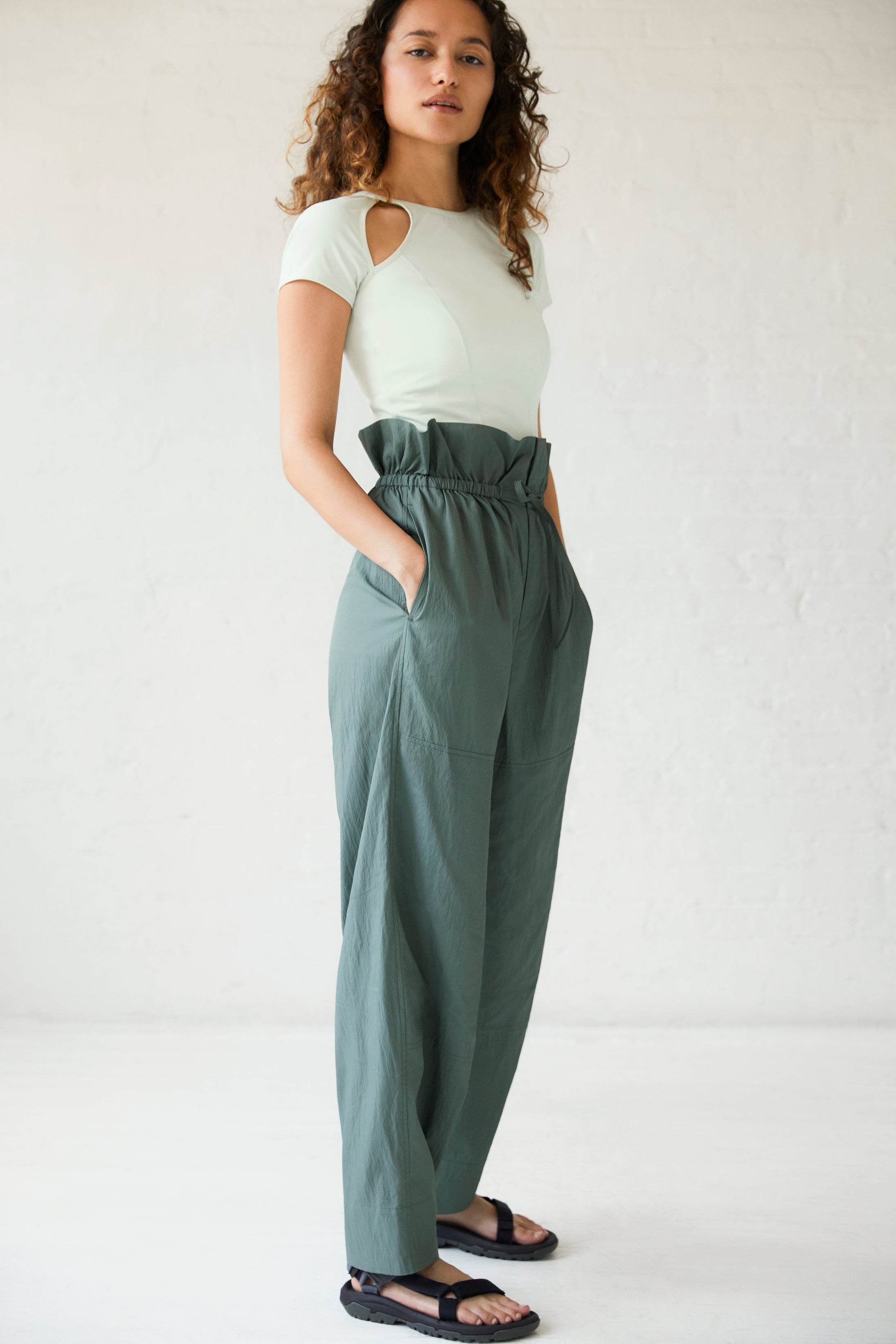 a woman wearing a white top and dark green pants and black sandals.