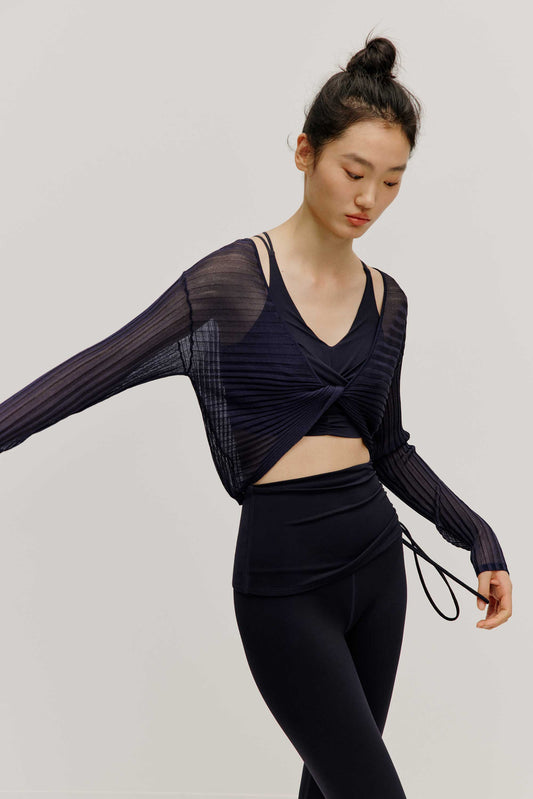 a woman wearing navy sports bra and leggings covered by a see-thru knit pull-over top.