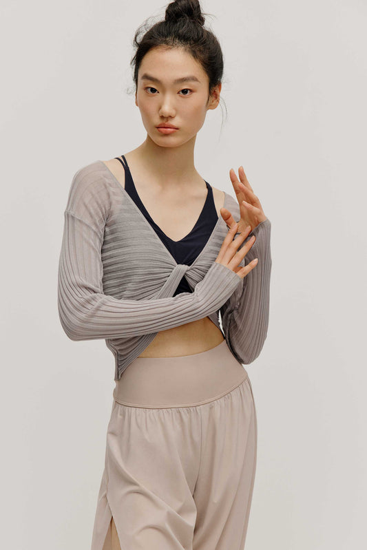 front view of a women wearing a neutral color woven jogger and a navy bra covered by a mauve color see thru knit top with a knot.