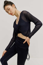 a woman wearing navy sports bra and leggings covered by a see-thru knit pull-over top.