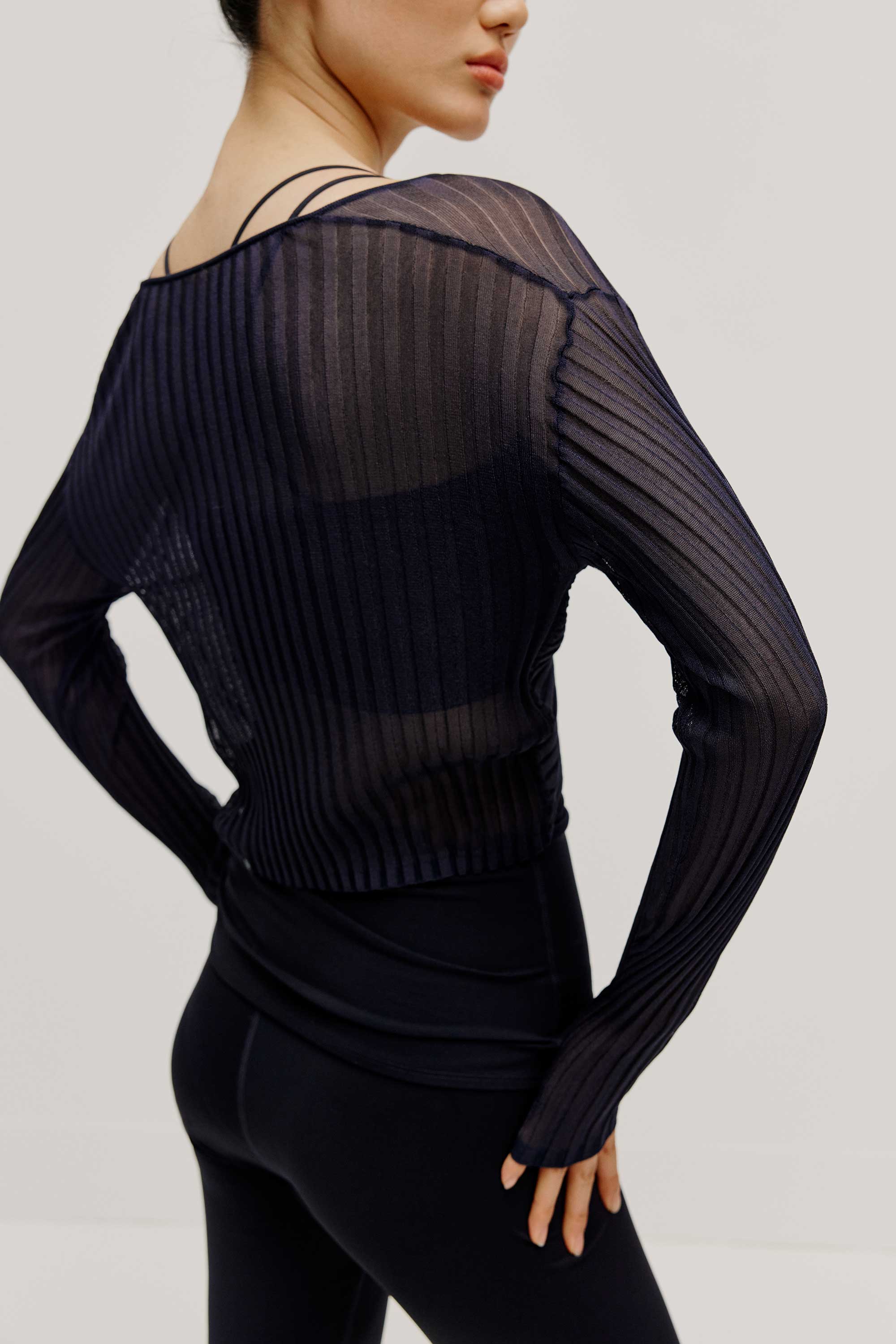 a woman wearing navy sports bra and leggings covered by a see-thru knit pull-over top.