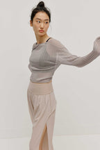 a women wearing a neutral color woven jogger and a navy bra covered by a mauve color see thru knit top.