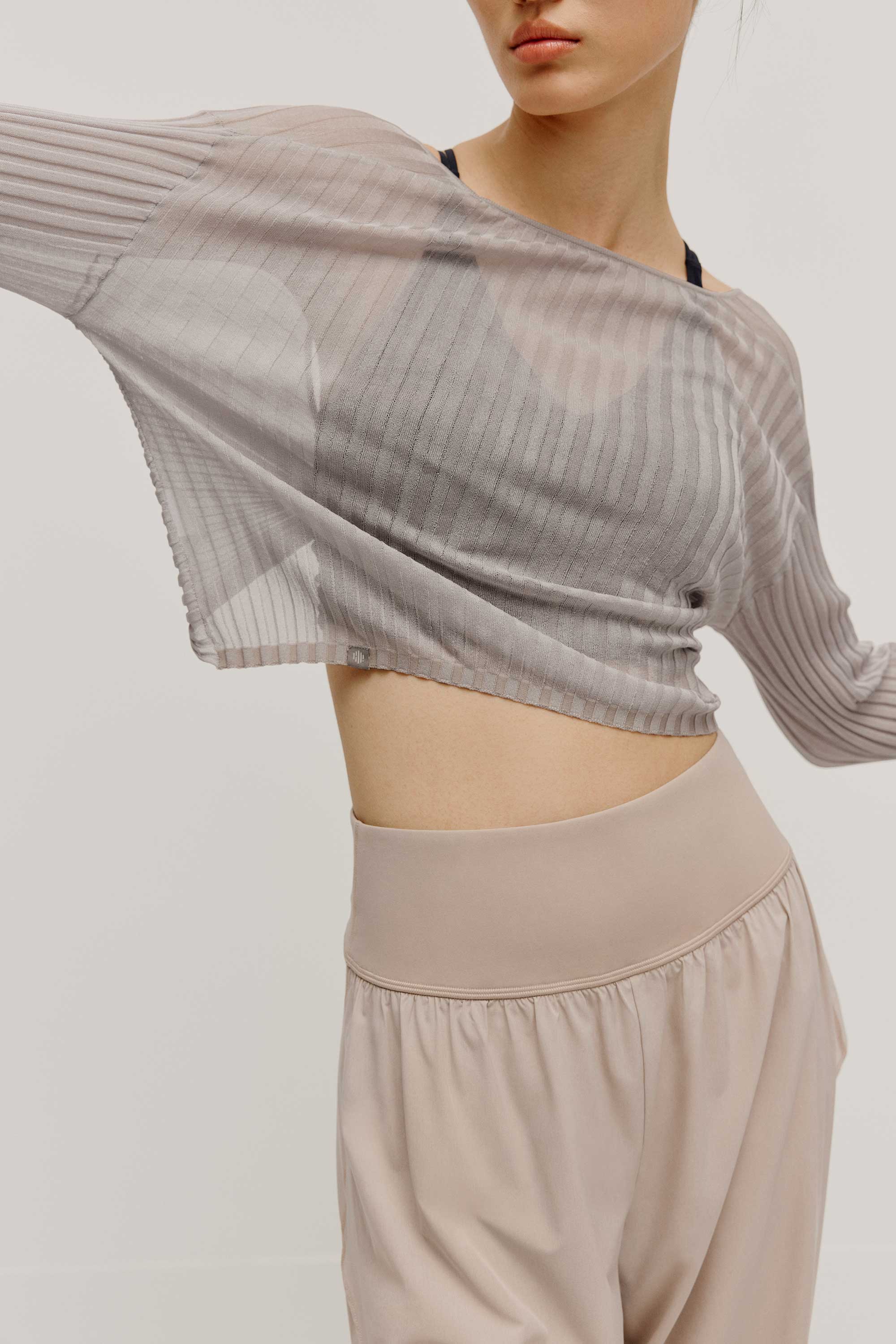 front view of a women wearing a neutral color woven jogger and a navy bra covered by a mauve color see thru knit top.