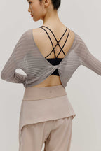 back view of a women wearing a neutral color woven jogger and a navy bra covered by a mauve color see thru knit top with a knot. 