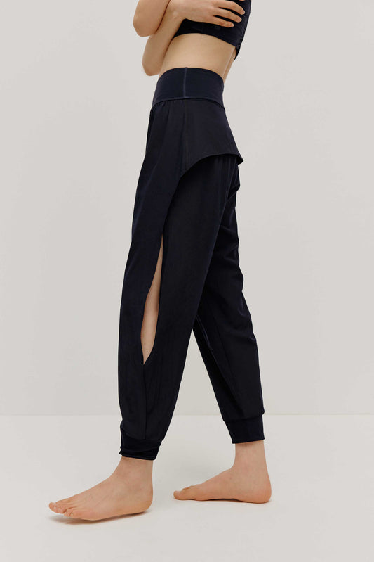 The side view of a woman wearing a pair of black tapered joggers with side slits 
