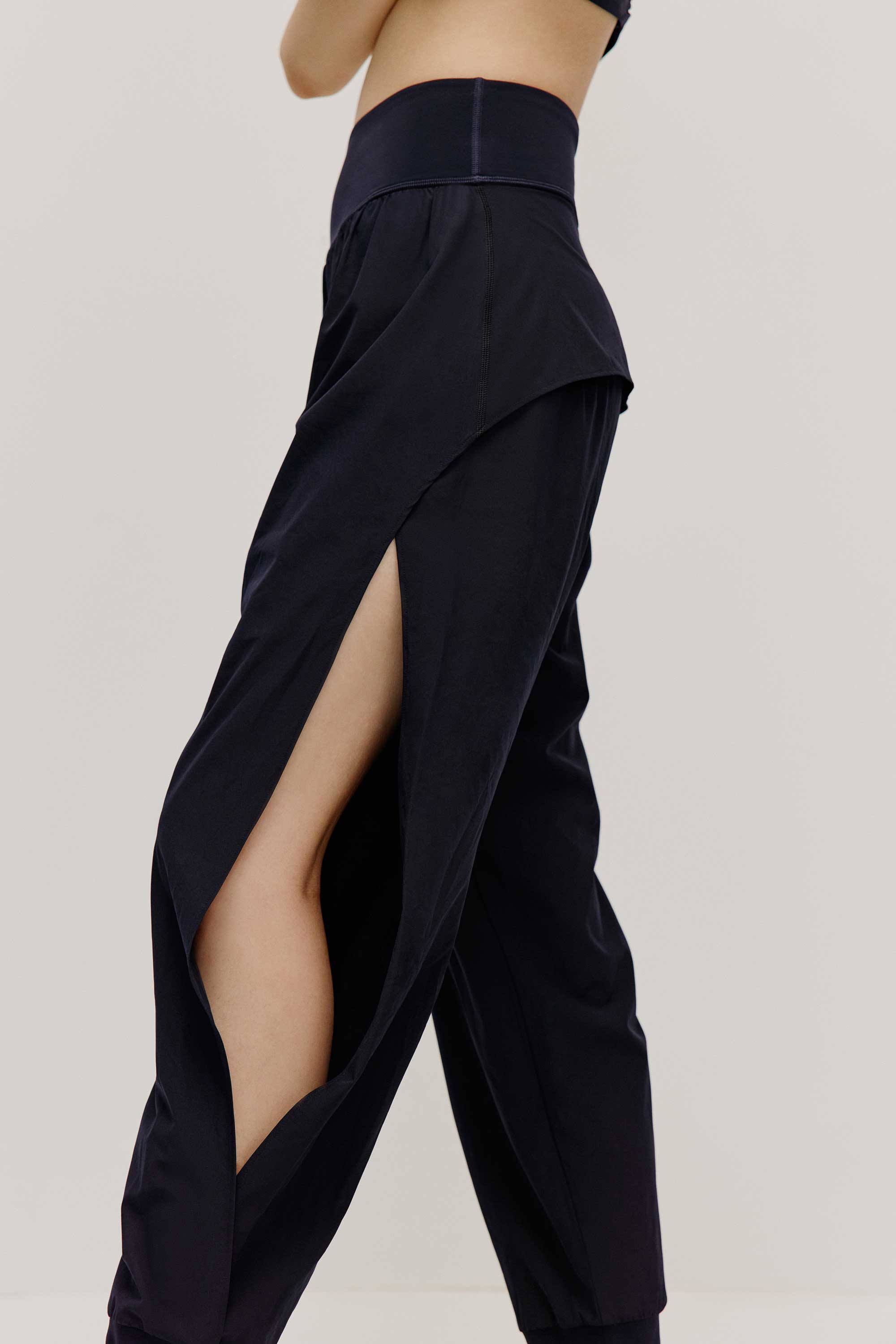 A close look of the side view of a woman wearing a pair of black tapered joggers with side slits