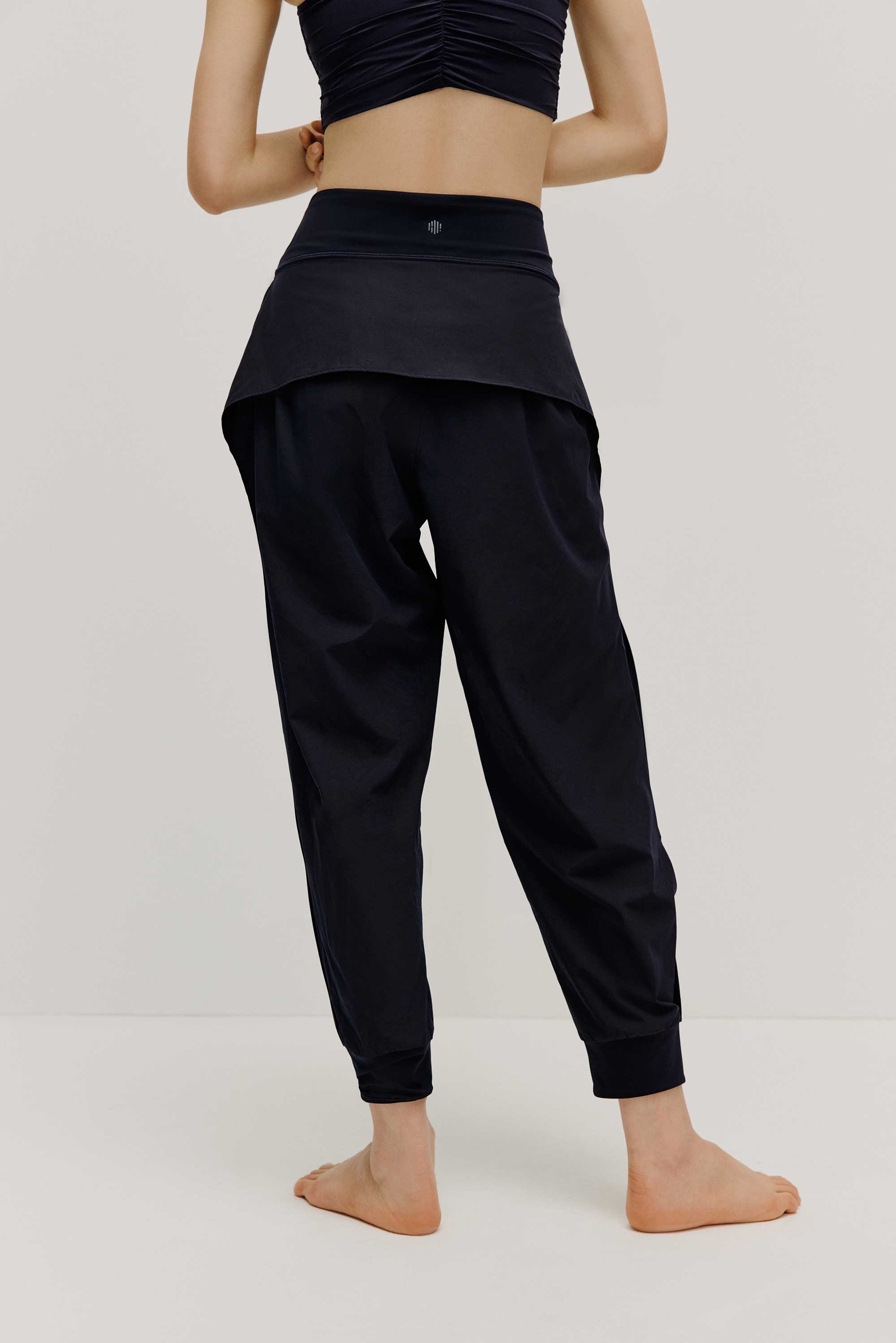 The back view of a model wearing black tapered joggers with NEIWAI Active logo on the waist