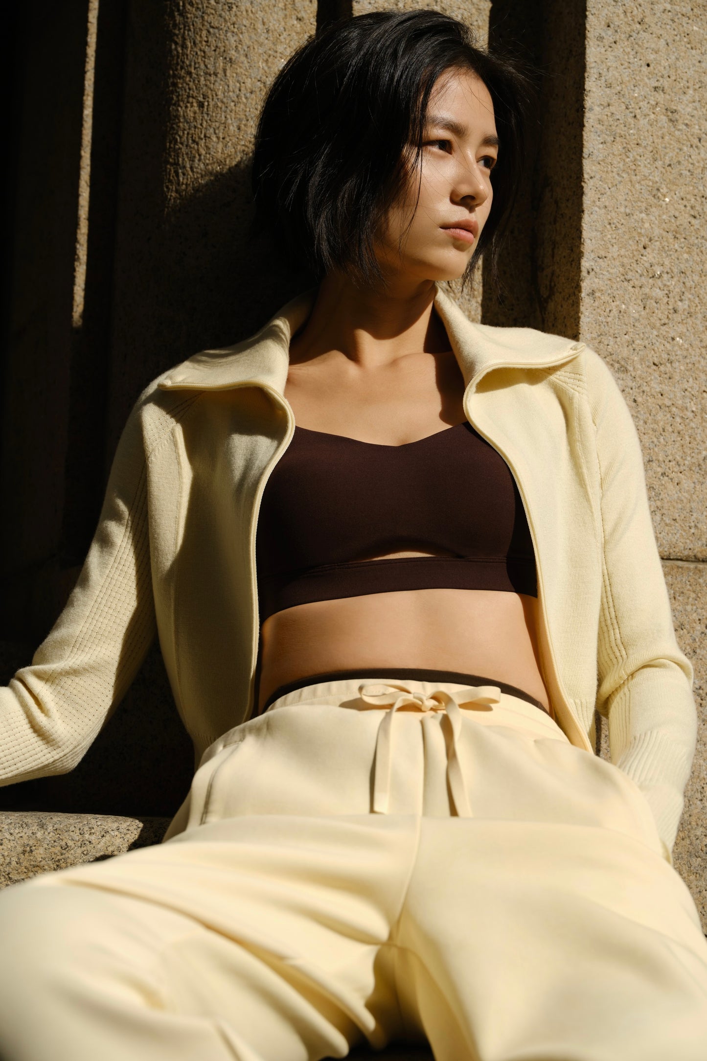 a woman wearing a white cardigan and white pants pair with a brown sports bra