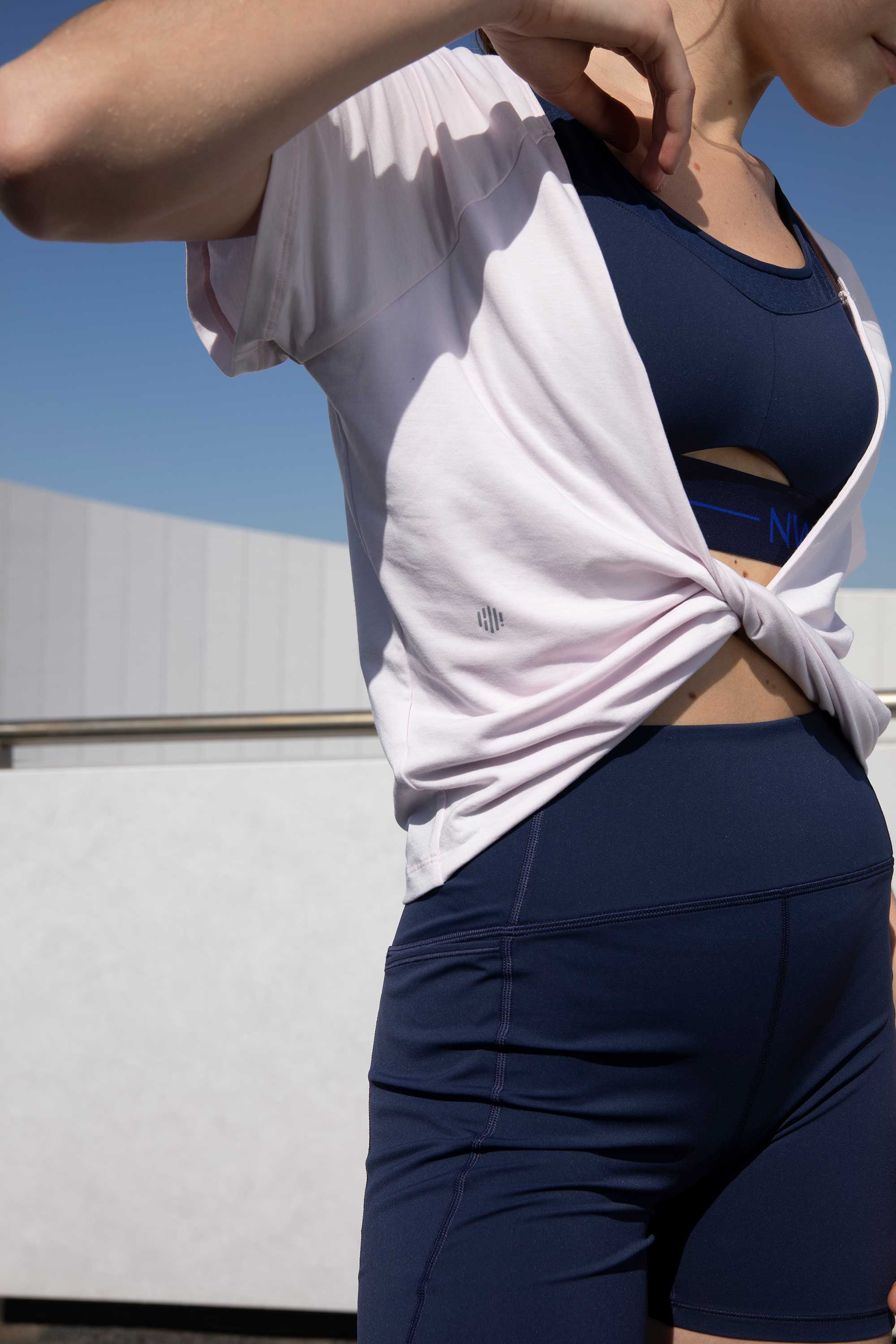 woman in pink t-shirt with front knot and navy sports bra and leggings