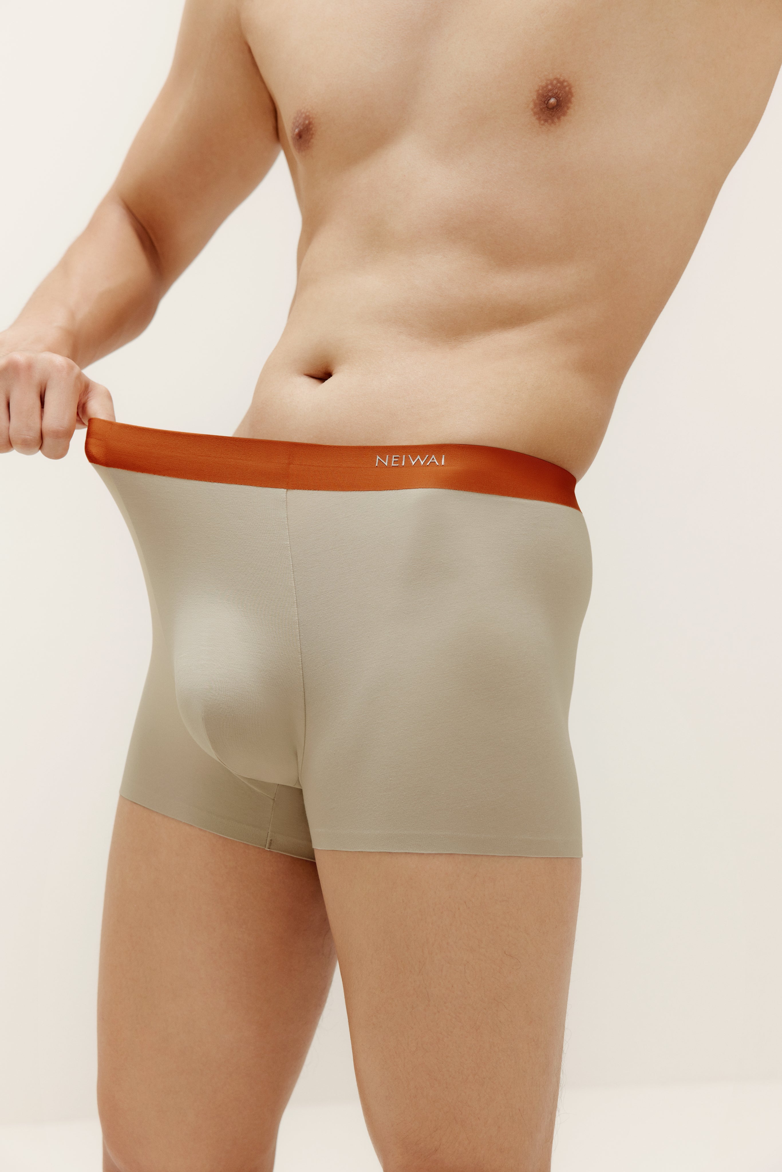 Closeup of man wearing beige boxer briefs with orange waistband. Oatmeal color. 