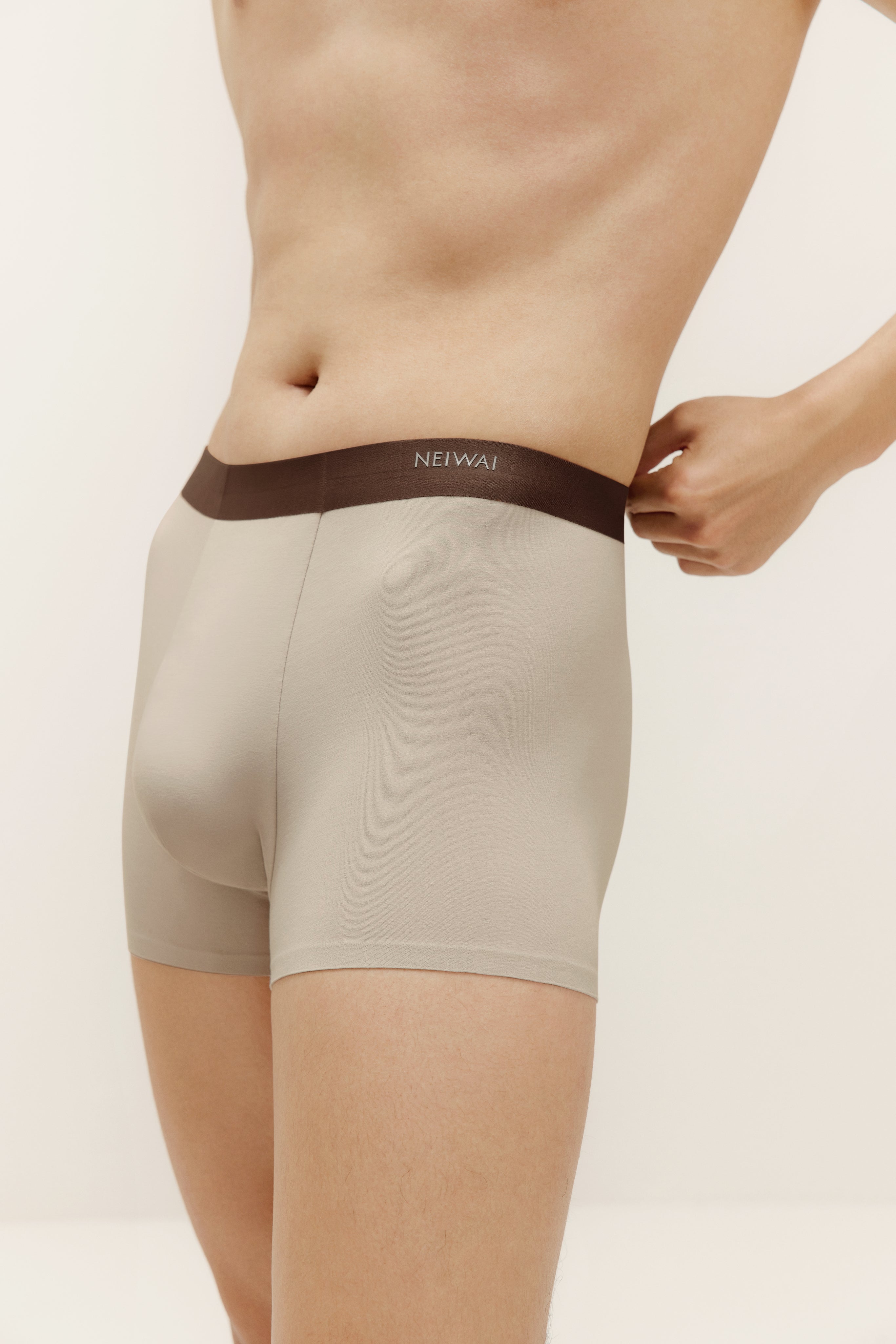 Closeup of man wearing tan boxer briefs with brown waistband. Light Heather color. 