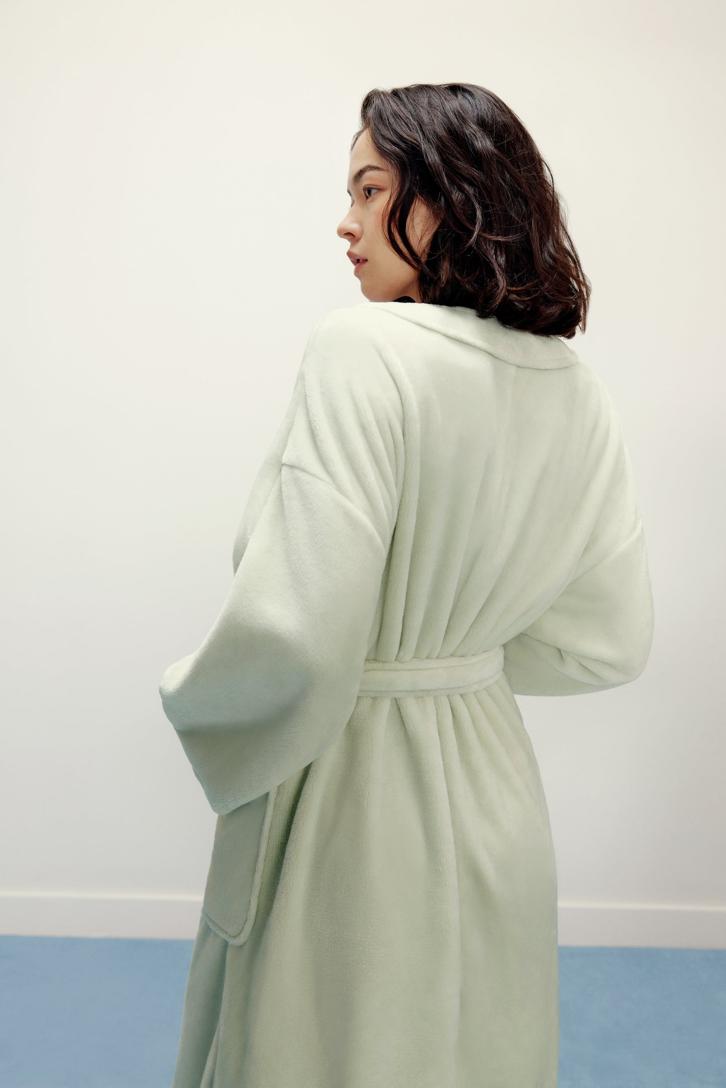 woman wearing a light green fleece robe back view 