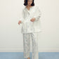 a woman wearing a white pajama sets with pattern and white slippers