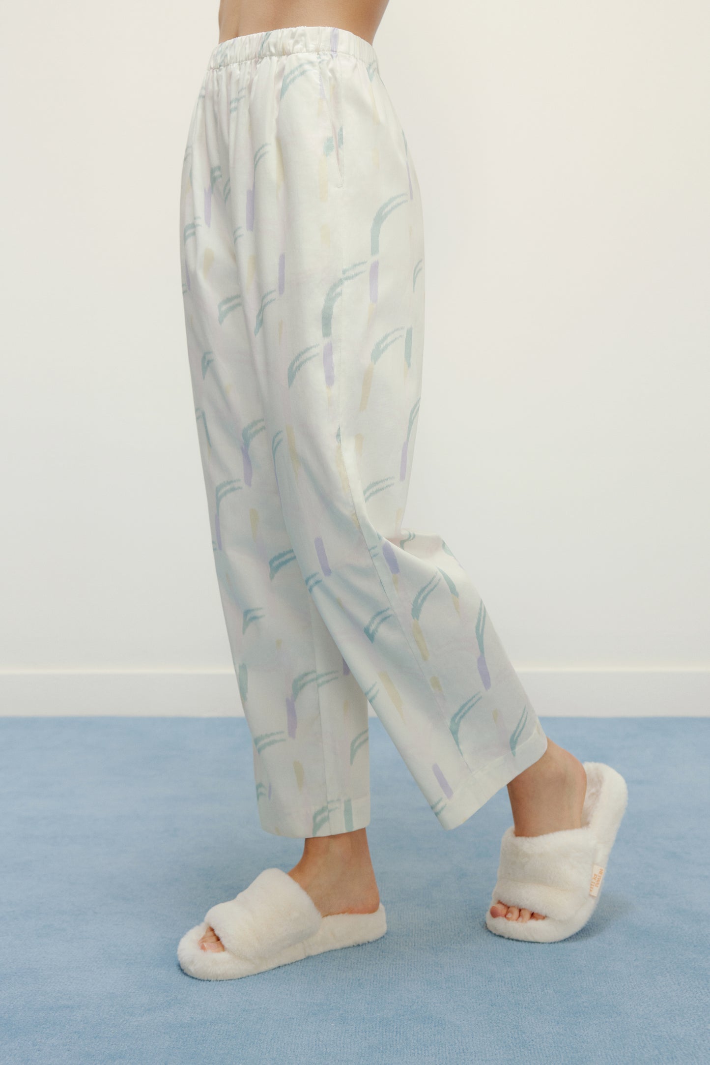 a person wearing a white pajama pants with pattern and white slippers 
