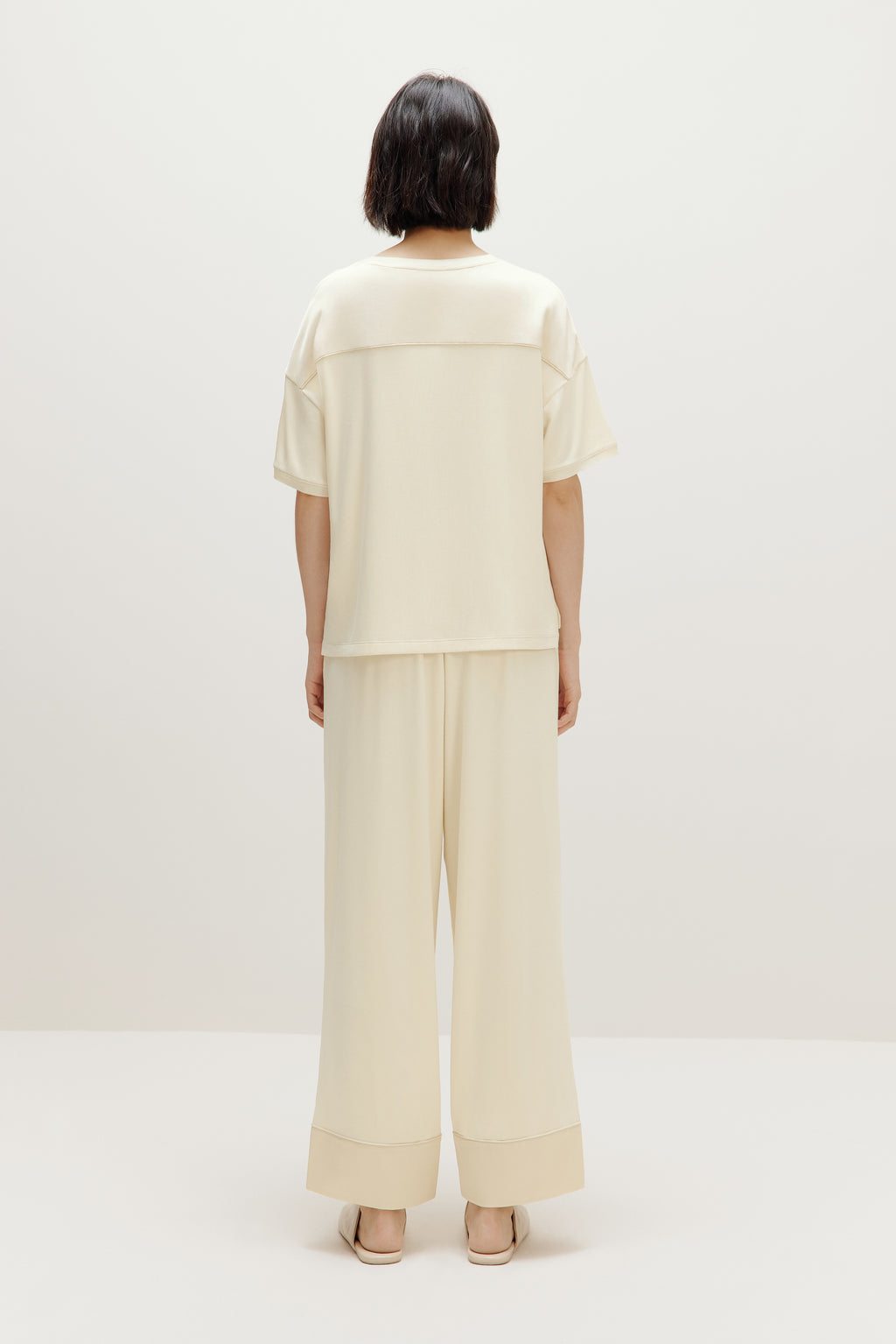 back of woman in cream pajama t-shirt and matching pants