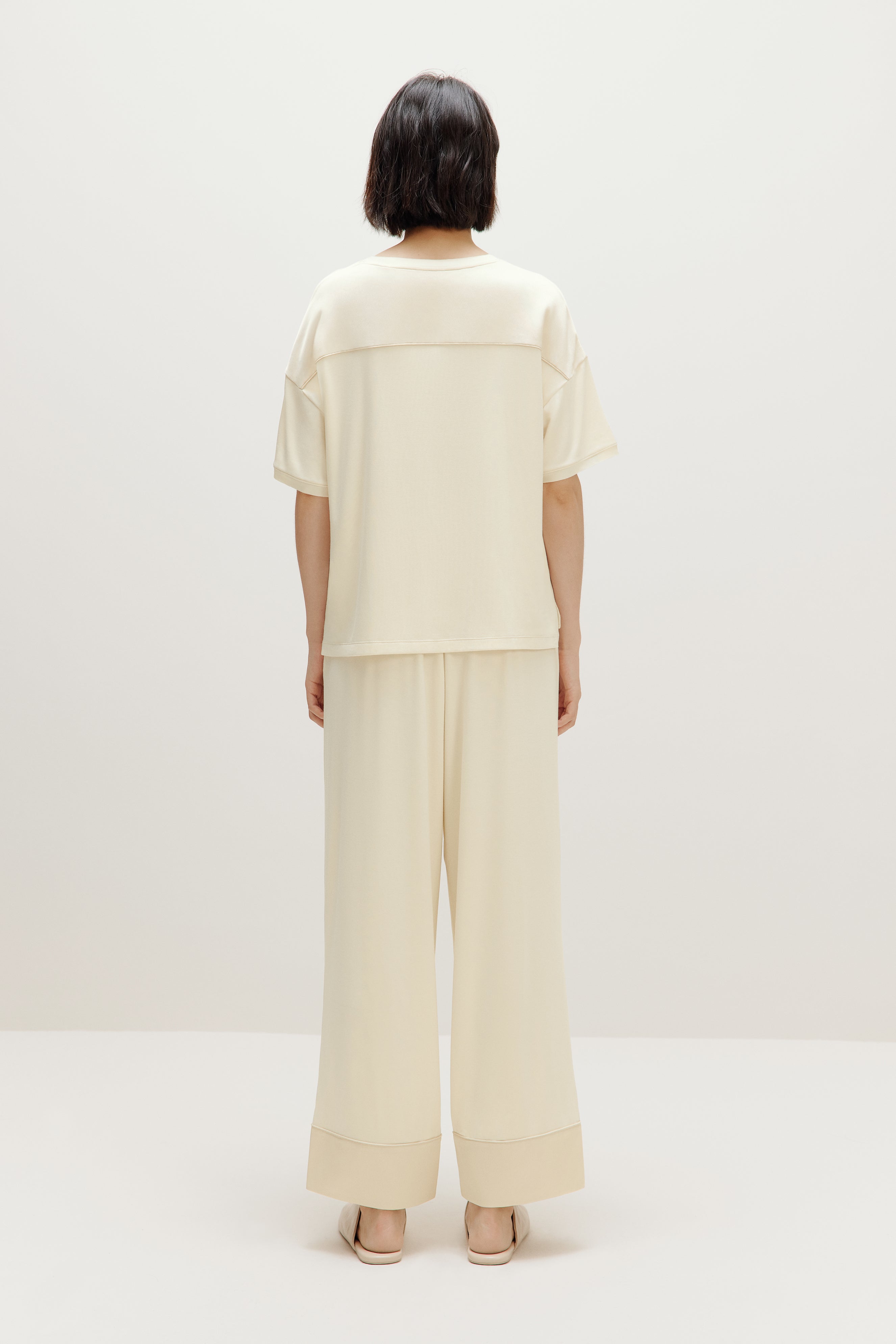 back of woman in cream pajama t-shirt and matching pants