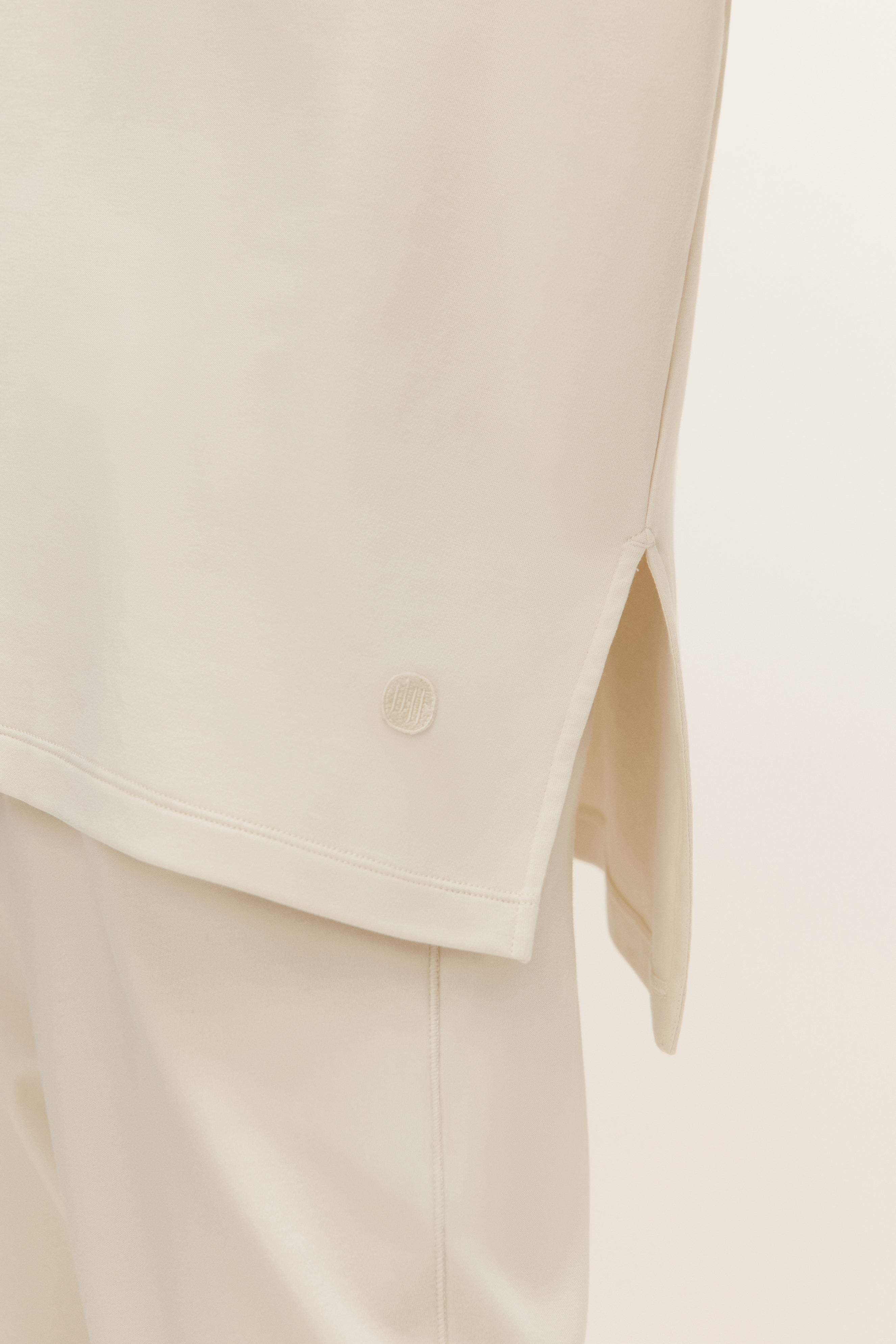 hem detail of the top showcasing the side slit and logo stitch.
